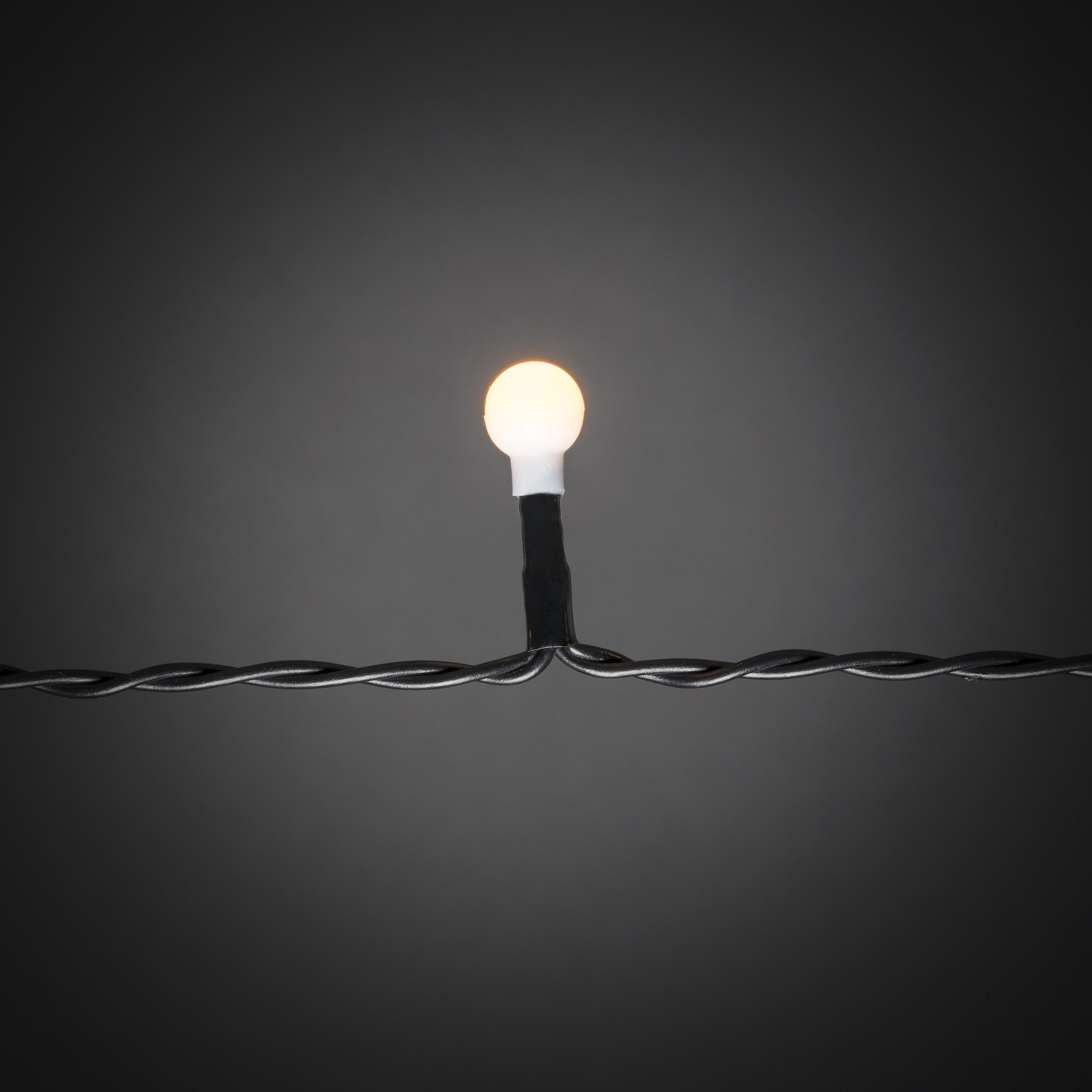 Eine einzelne leuchtende Weihnachtslichterkette. Die Glühbirne ist weiß vor dunklem Hintergrund. Ein schwarzes Kabel liegt darunter.