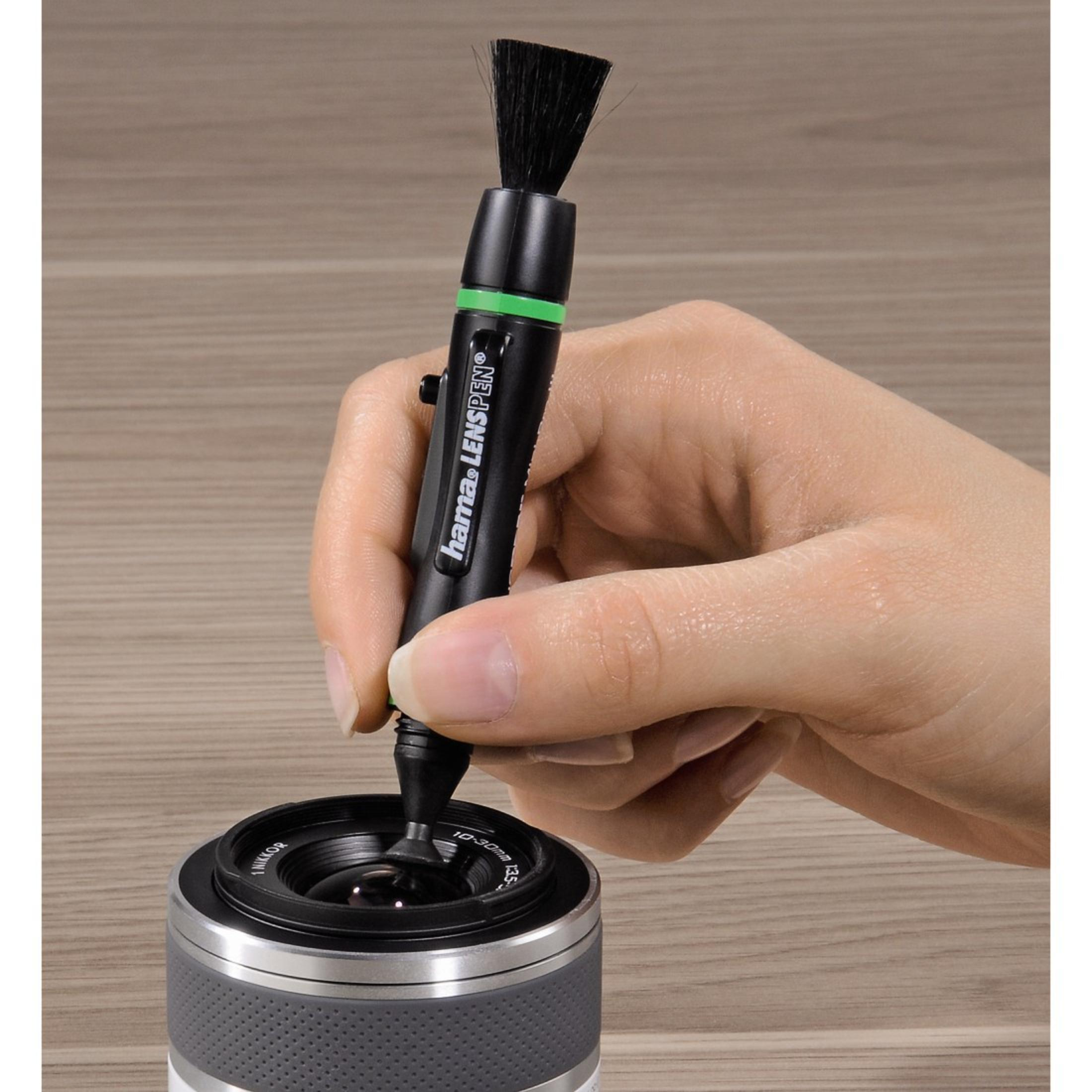 Hand verwendet einen Objektiv-Reinigungsstift, um ein Kameraobjektiv zu reinigen, wobei der Markenname sichtbar ist.