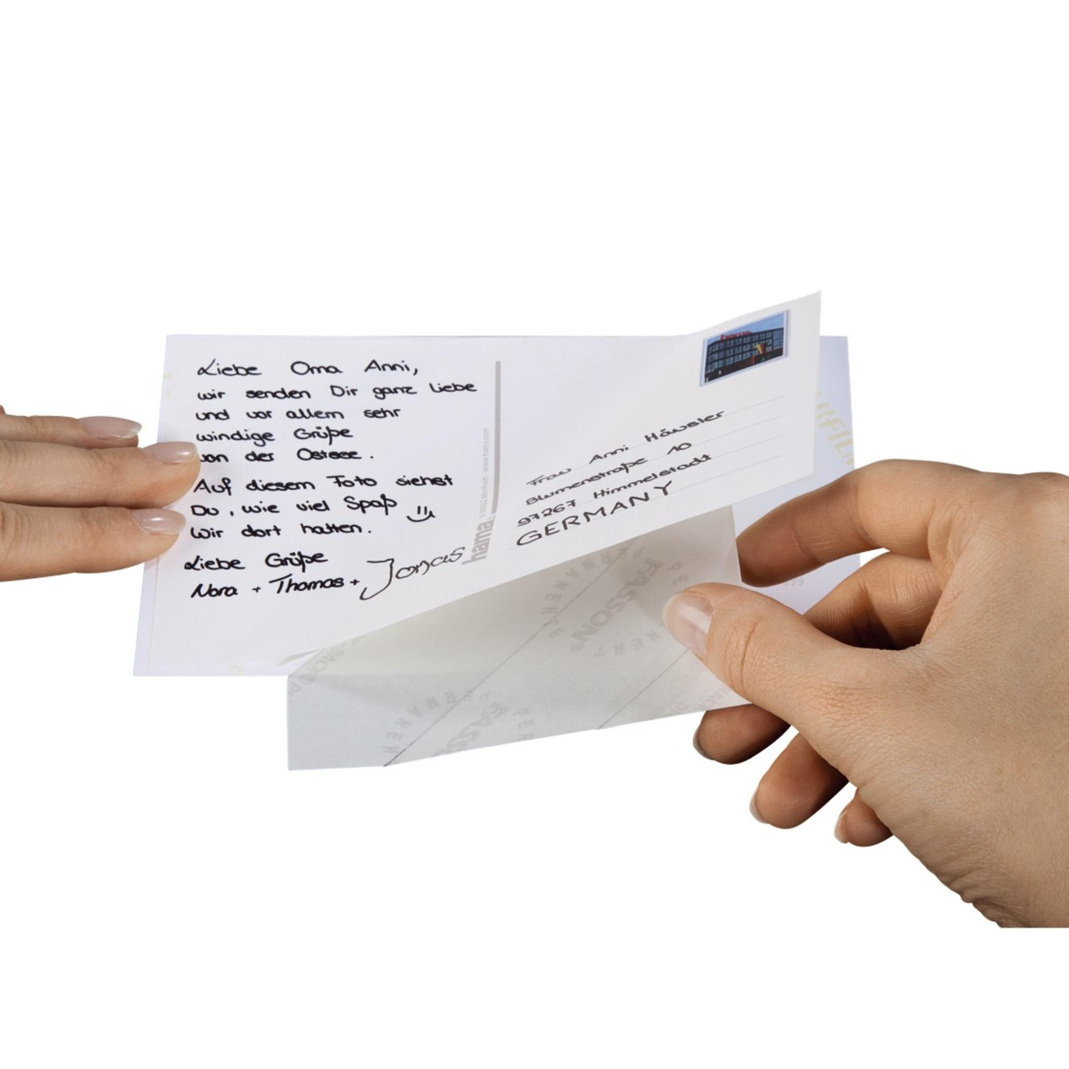 Le mani tengono una cartolina con testo scritto a mano e un'immagine parzialmente visibile sul retro.