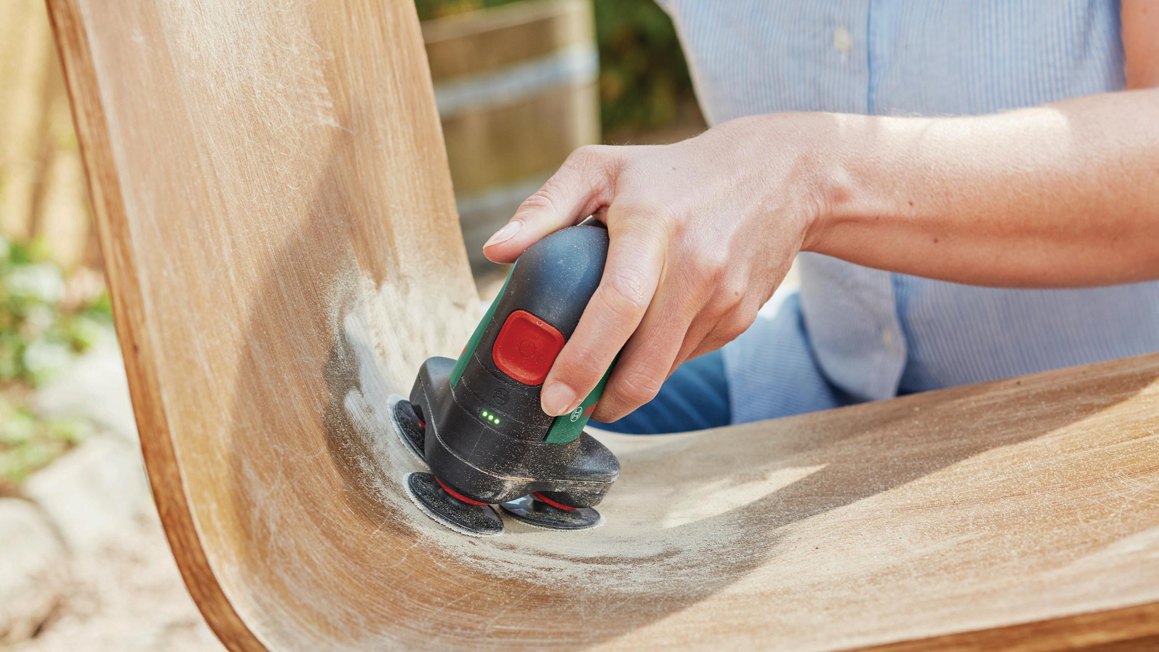 Nahaufnahme einer Hand, die mit einem Elektrowerkzeug eine gebogene Holzoberfläche abschleift, wobei die Präzision und Kontrolle des Werkzeugs hervorgehoben werden.