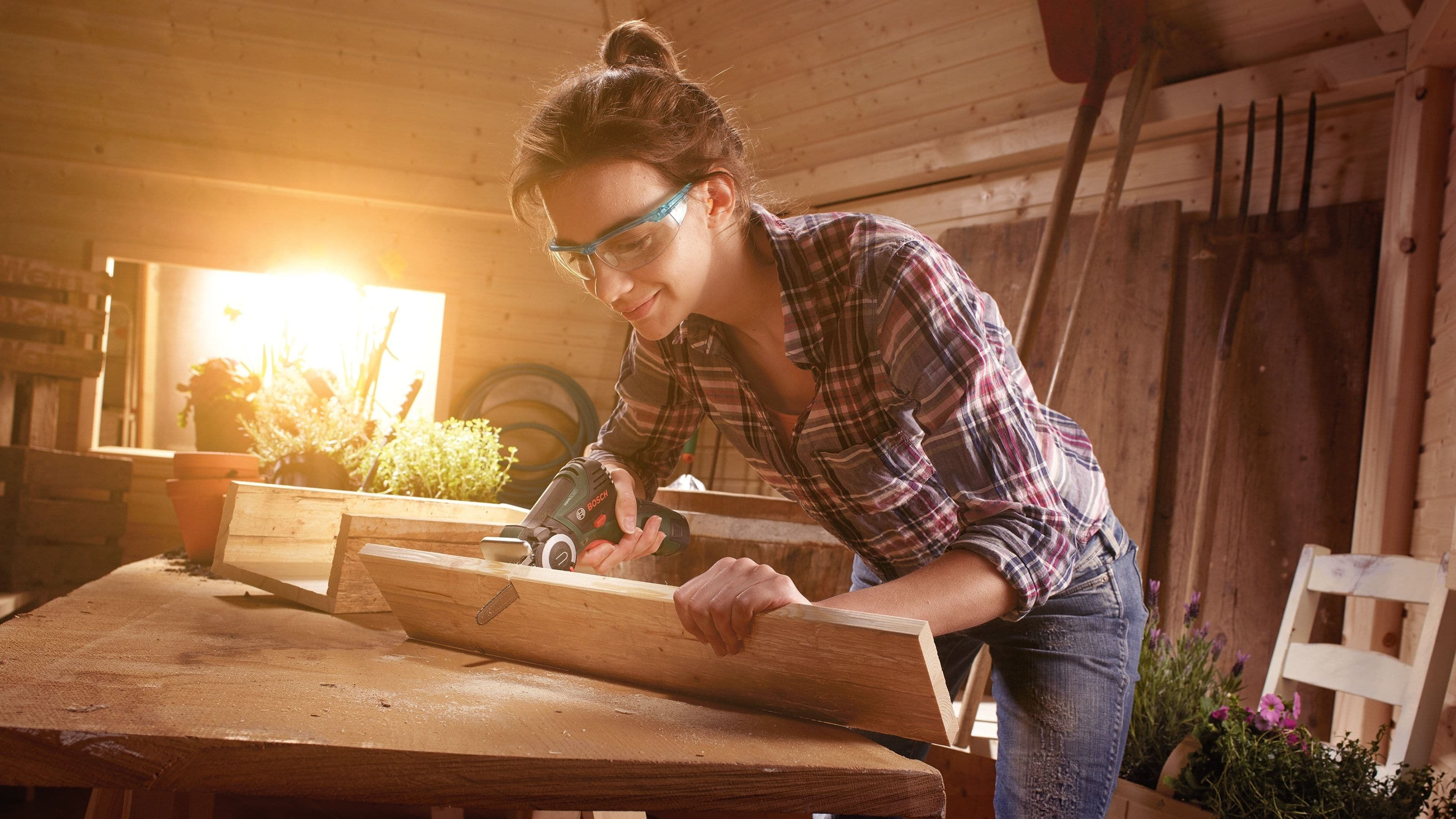 Eine Frau schneidet Holz mit einer Bosch EasyCut 12 nanoBLADE Säge in einer sonnendurchfluteten Werkstatt.