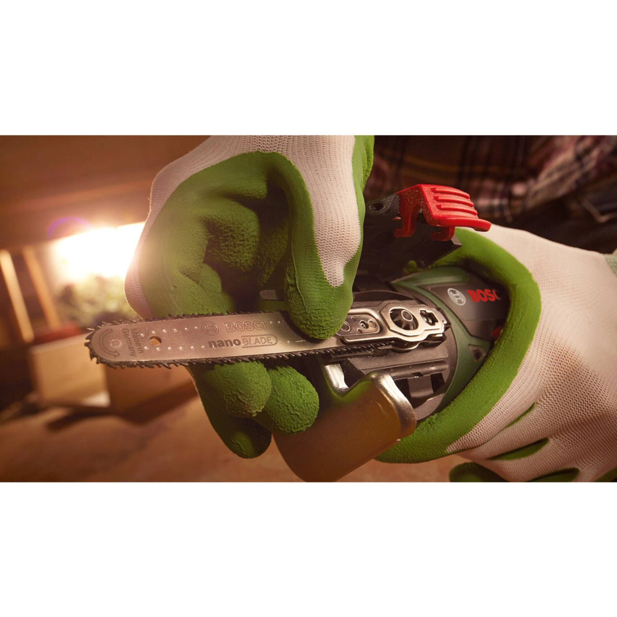 Eine Hand in einem grünen Handschuh hält eine Bosch EasyCut 12 nanoBLADE Säge, aus nächster Nähe.
