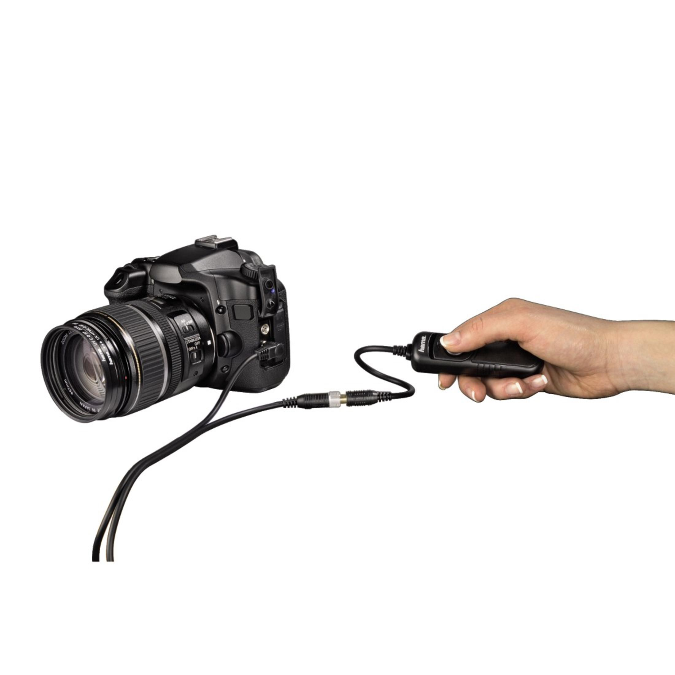 A camera is connected to a remote control in a hand, against a white background.