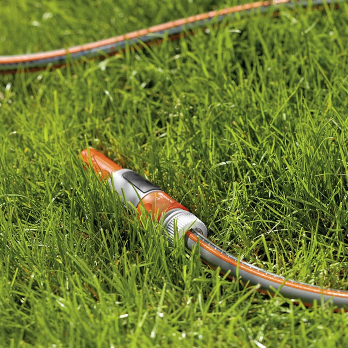 Ein orangefarbener und grauer Schlauch mit Düse liegt auf grünem Gras. Im Hintergrund mehr Schlauch und Gras.