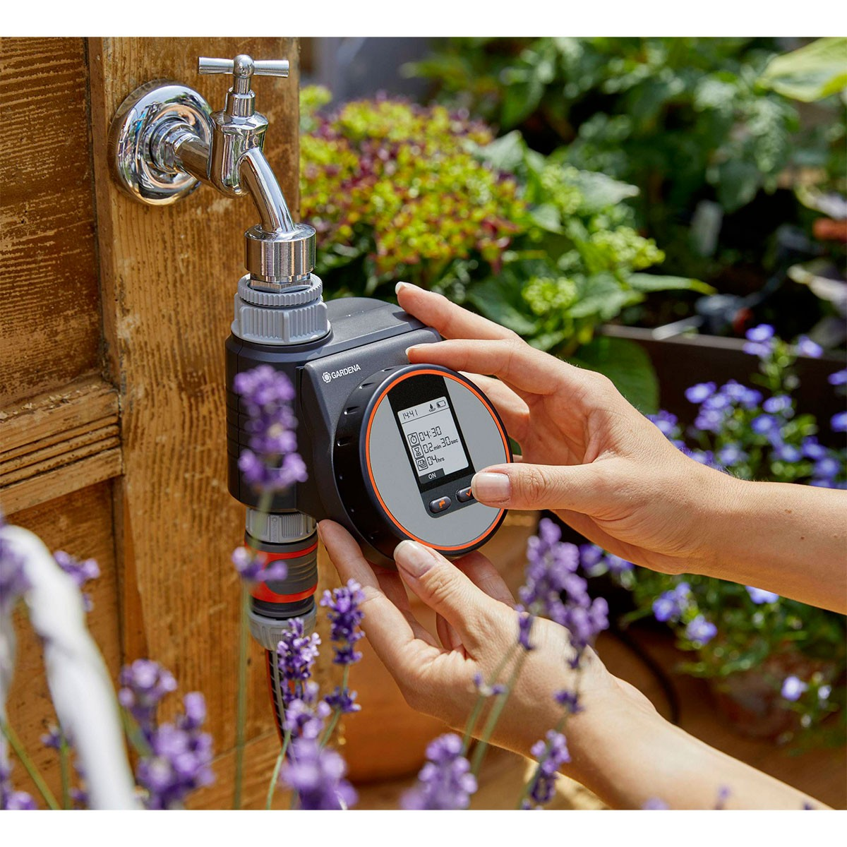 Ein Gardena-Bewässerungstimer an einem Wasserhahn befestigt. Hände justieren den Timer.