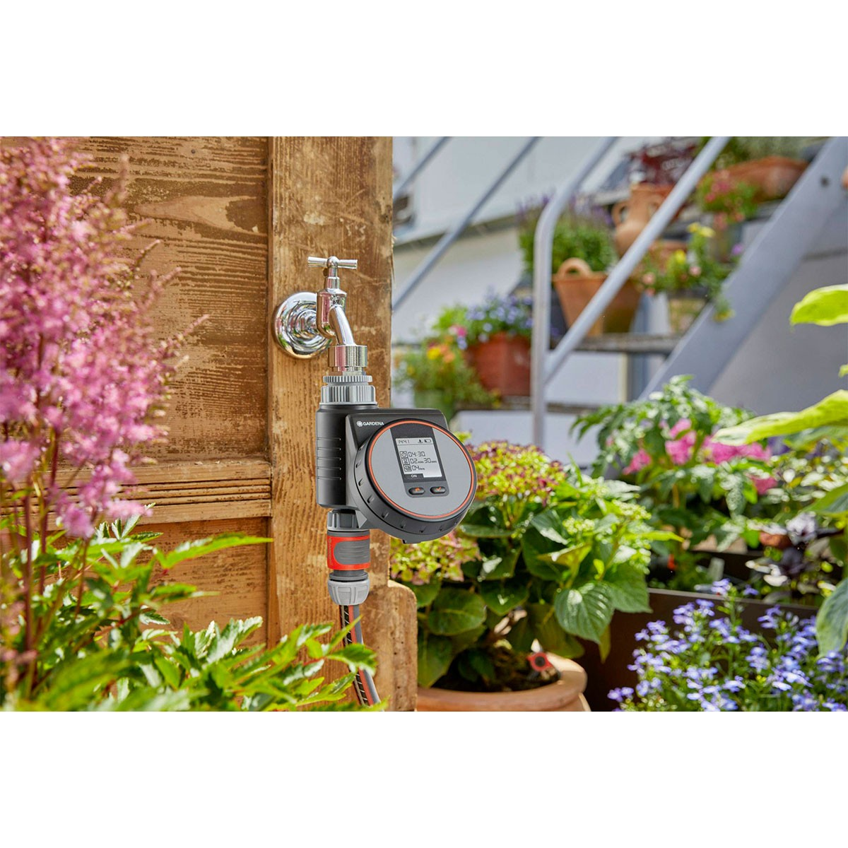Gardena-Bewässerungstimer an einem Wasserhahn befestigt. Blumen und Laub im Hintergrund.