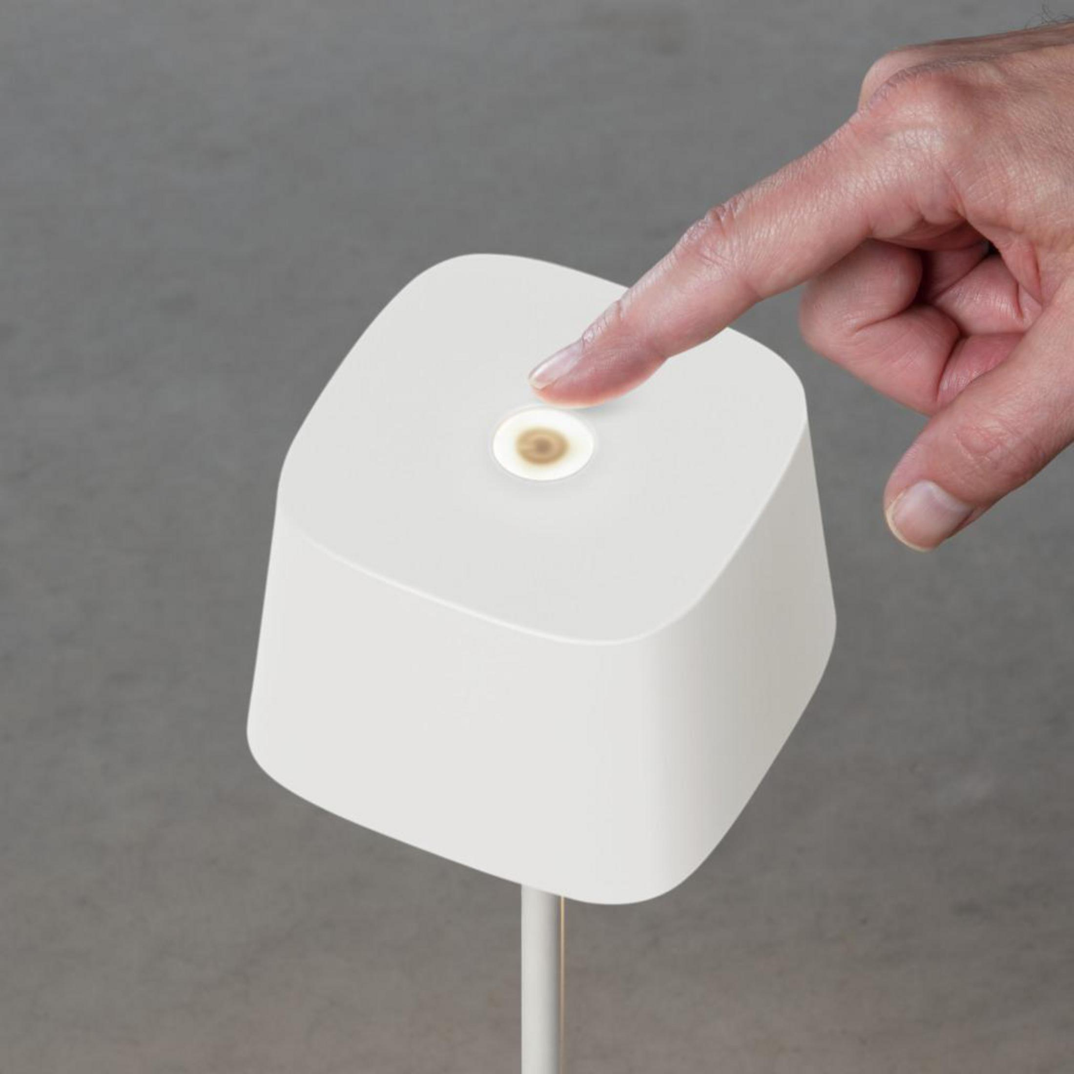 Ein Finger berührt den Ein-/Ausschalter einer weißen Lampe mit quadratischem Sockel.