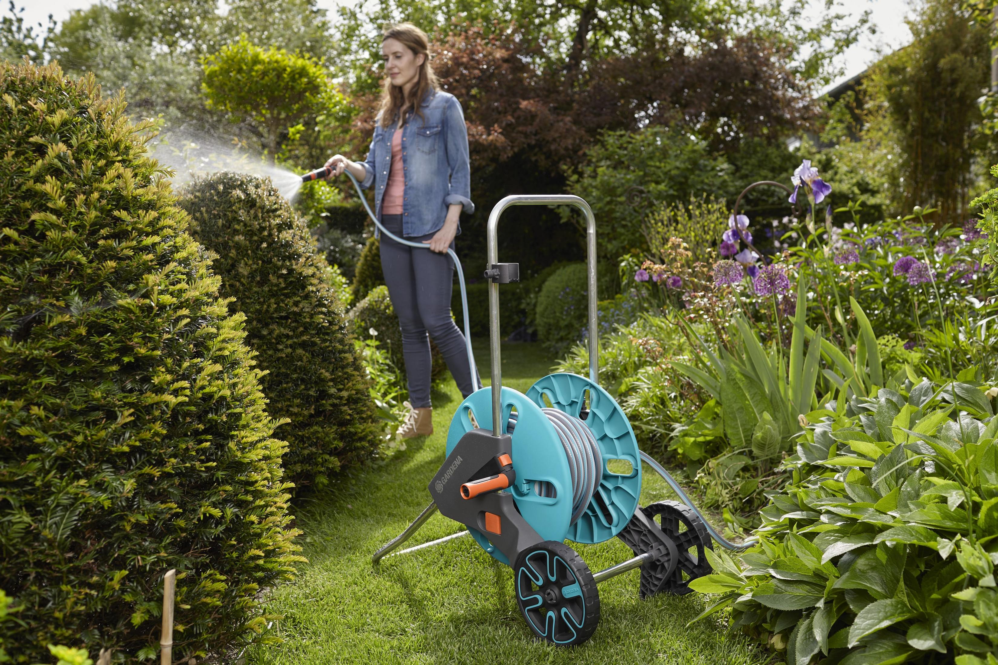 Frau verwendet eine Gardena Schlauchhaspel, um Pflanzen in einer üppigen Gartenanlage zu bewässern.
