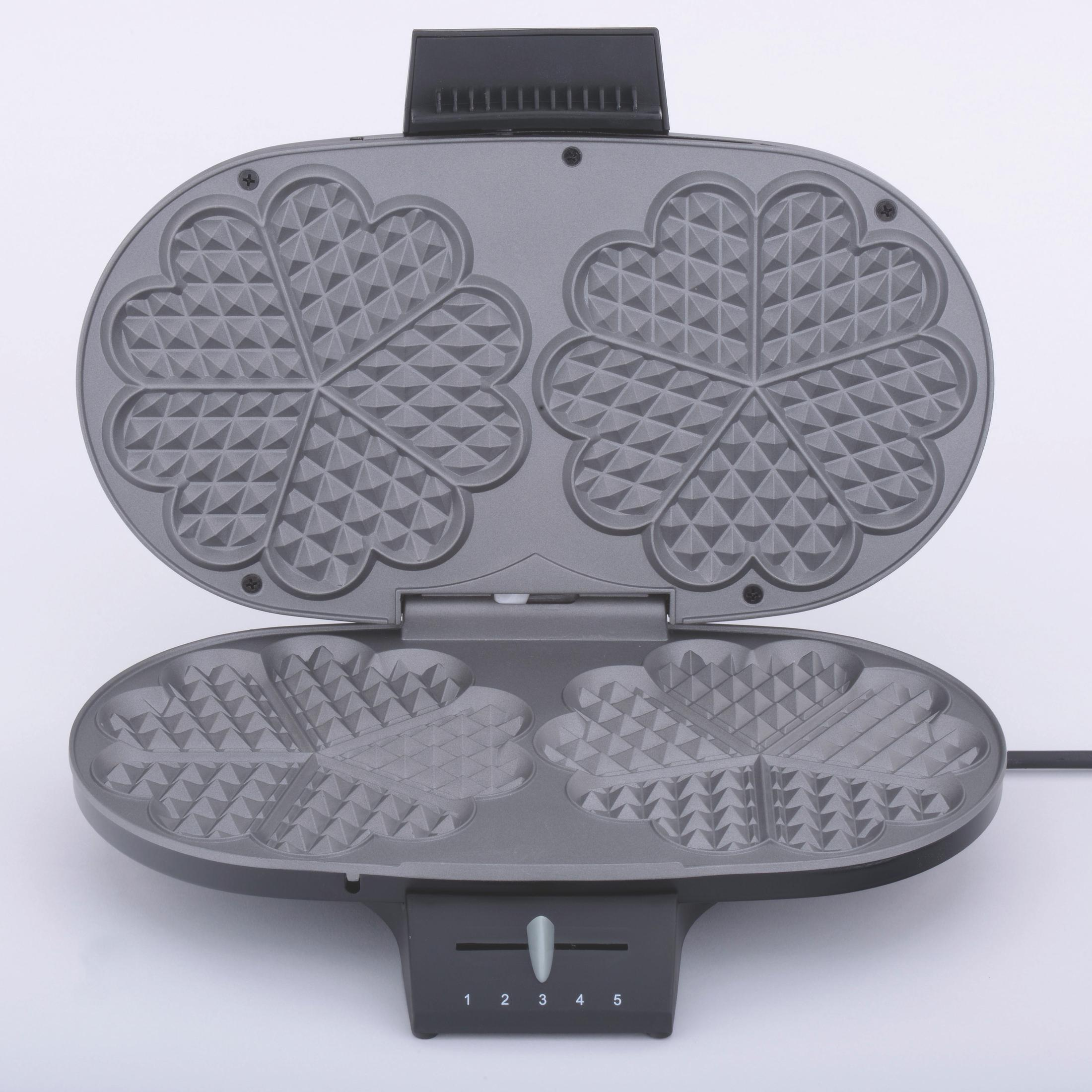 Otwarta szara gofrownica z formami w kształcie serca stoi na białej powierzchni.