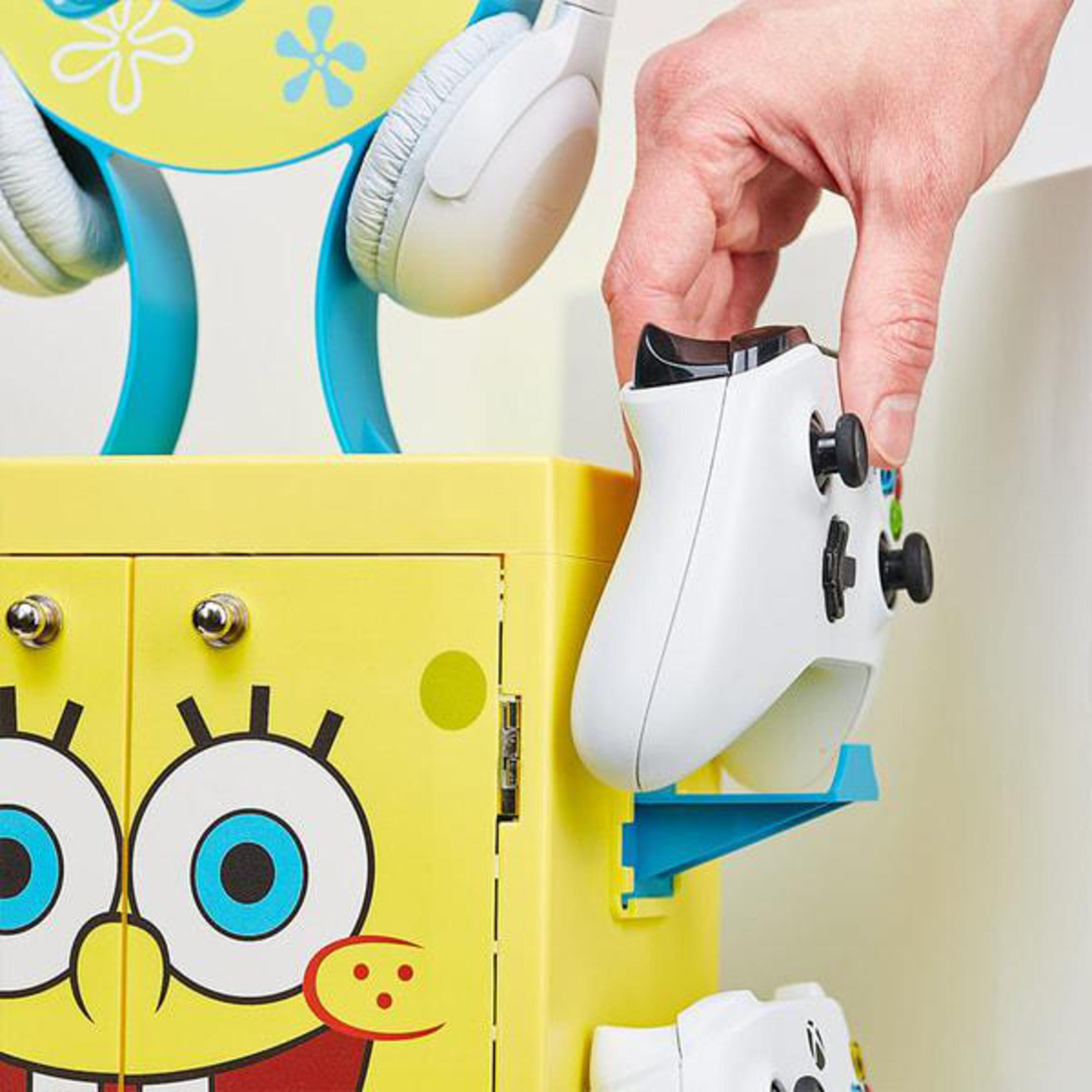 Mano che posiziona un gamepad bianco su un organizzatore giallo di SpongeBob SquarePants con accenti blu, in una stanza.