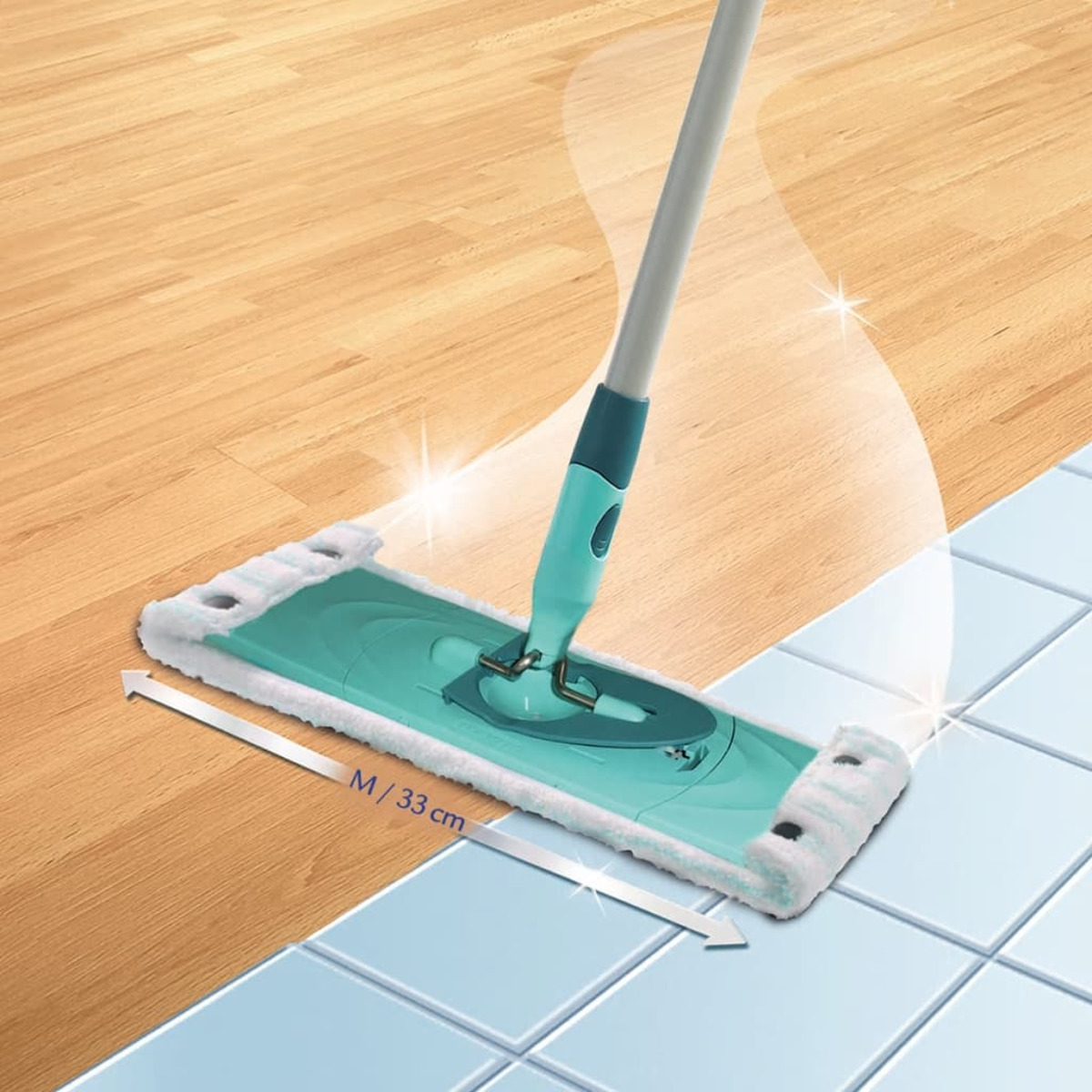 Un mocio sta pulendo una superficie che passa da un pavimento in legno a un pavimento piastrellato blu. C'è una freccia con del testo.