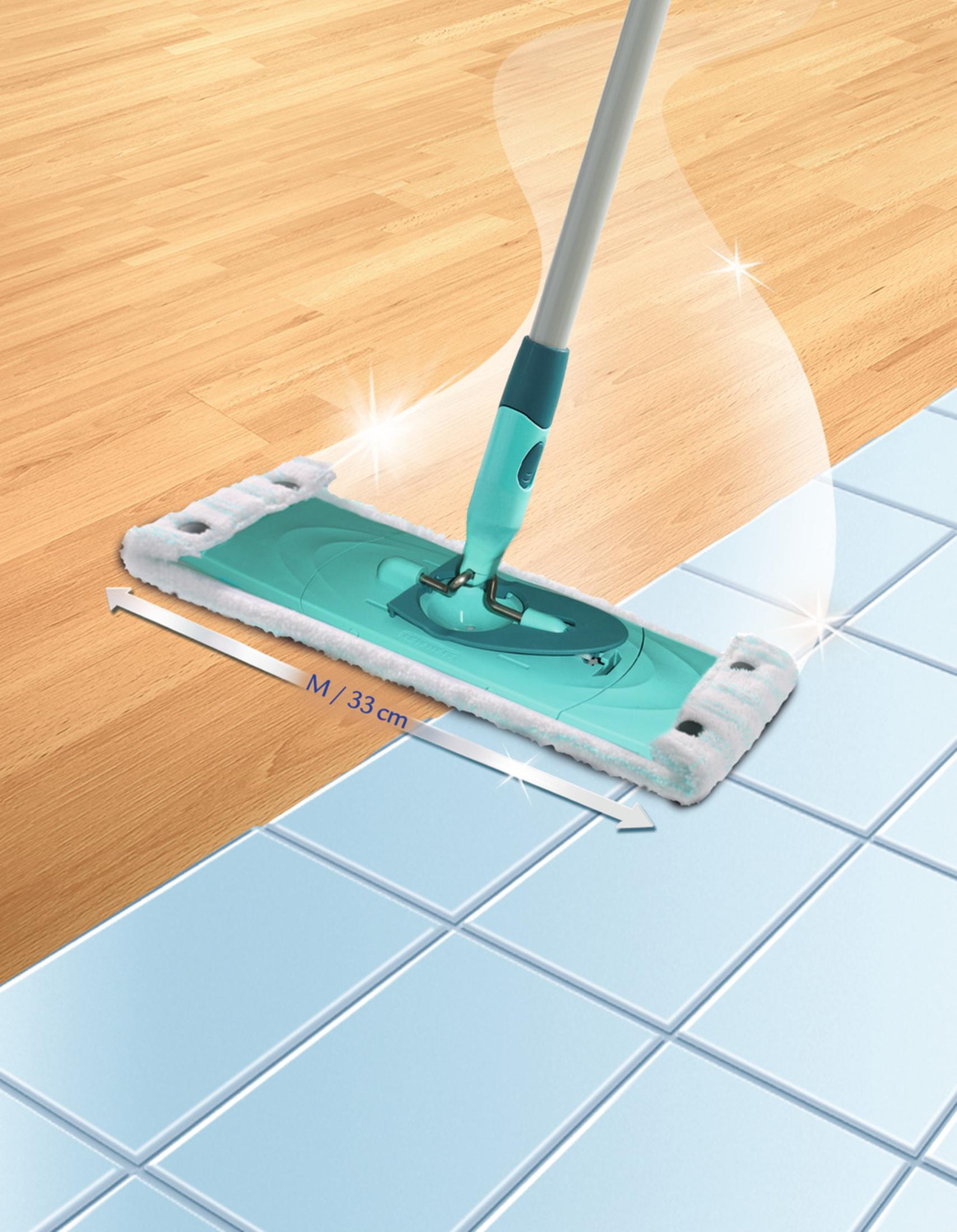 Un mocio sta pulendo una superficie che passa da un pavimento in legno a un pavimento piastrellato blu. C'è una freccia con del testo.