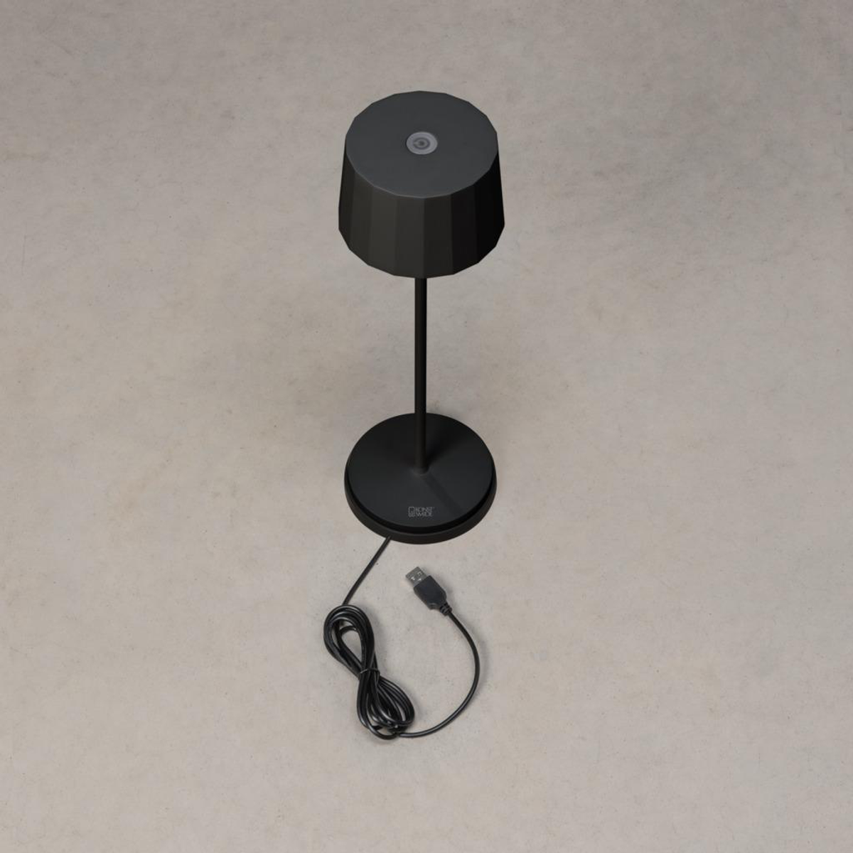 Eine schwarze Lampe mit einem USB-Ladekabel wird auf einer grauen Oberfläche gezeigt, wobei das Design und die Ladefunktion aus der Vogelperspektive hervorgehoben werden.