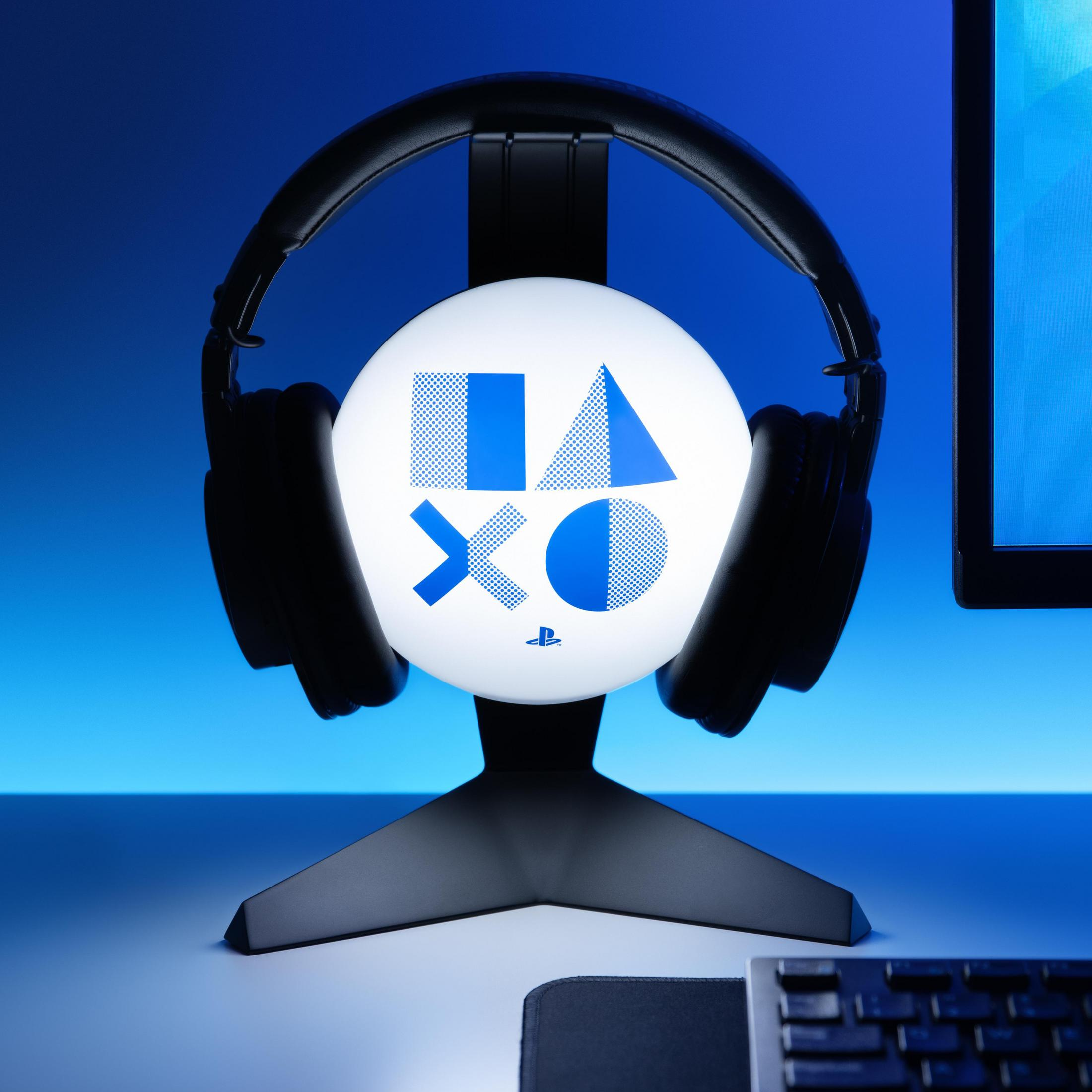 Lampa czołowa PlayStation na czarnym stojaku podtrzymuje czarne słuchawki, wyświetlając logo PlayStation w kolorze niebiesko-białym.