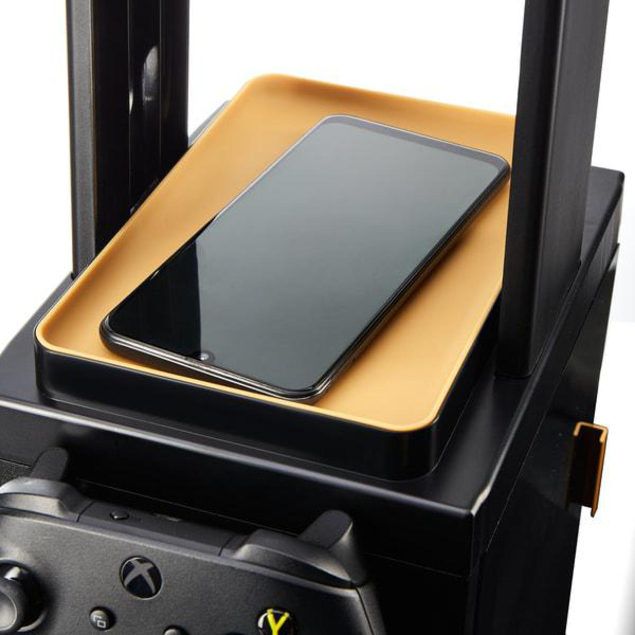 Primo piano di uno smartphone nero su un vassoio dorato, sopra un supporto da gioco nero.