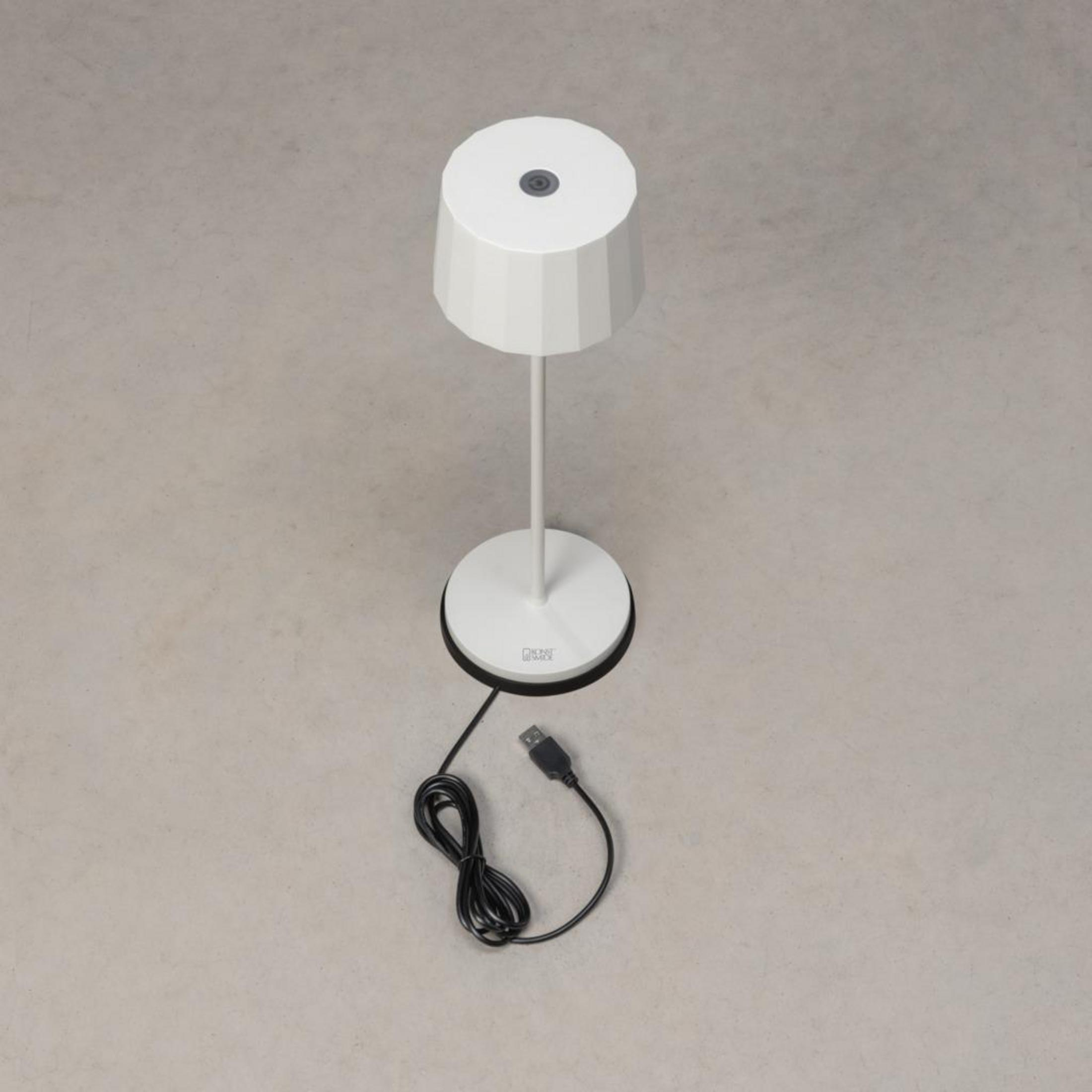Eine weiße Stehlampe mit rundem Fuß und zylindrischem Schirm mit einem Ladekabel auf grauem Hintergrund.