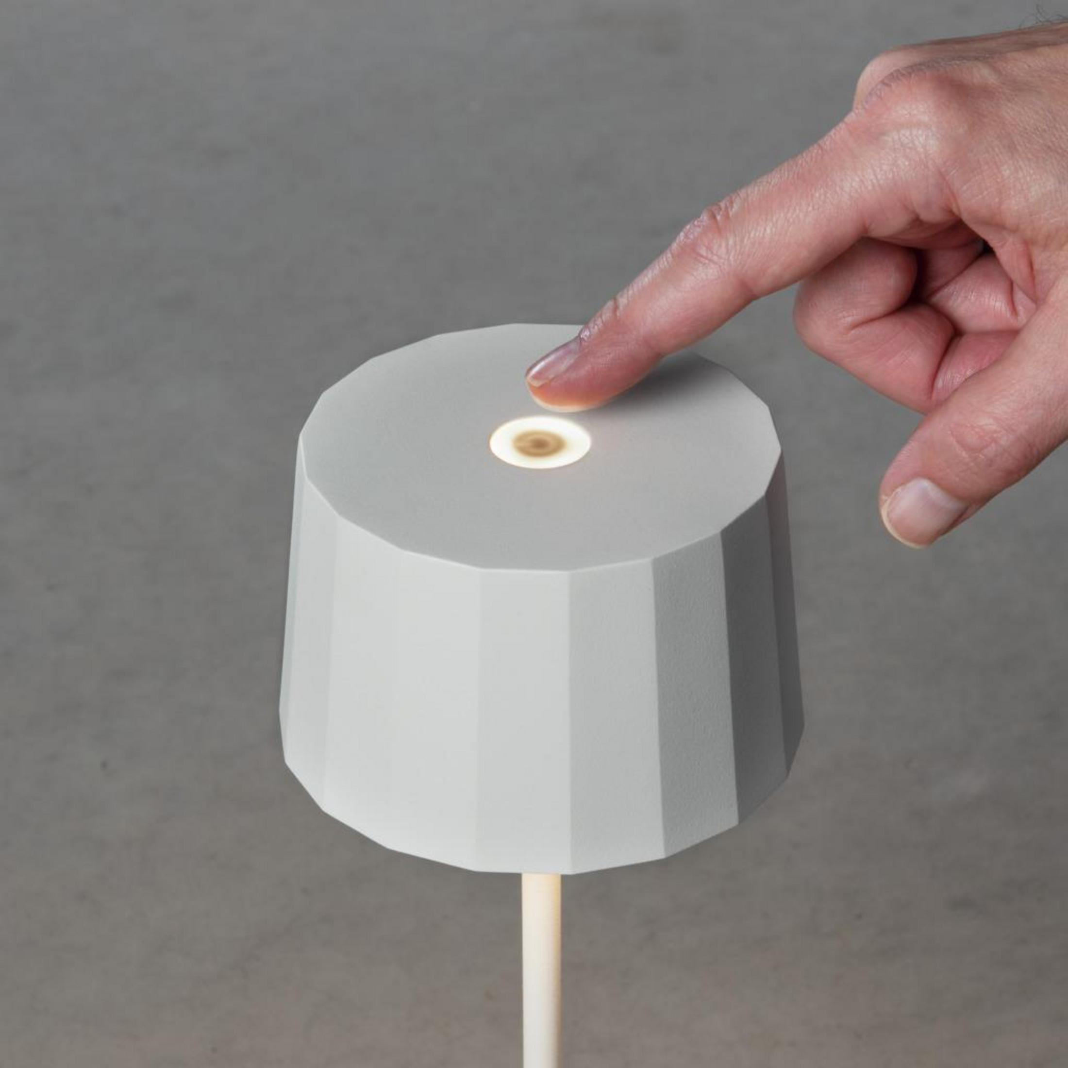 Ein Finger drückt auf die Oberseite einer weißen Stehlampe mit rundem Fuß und zylindrischem Schirm.