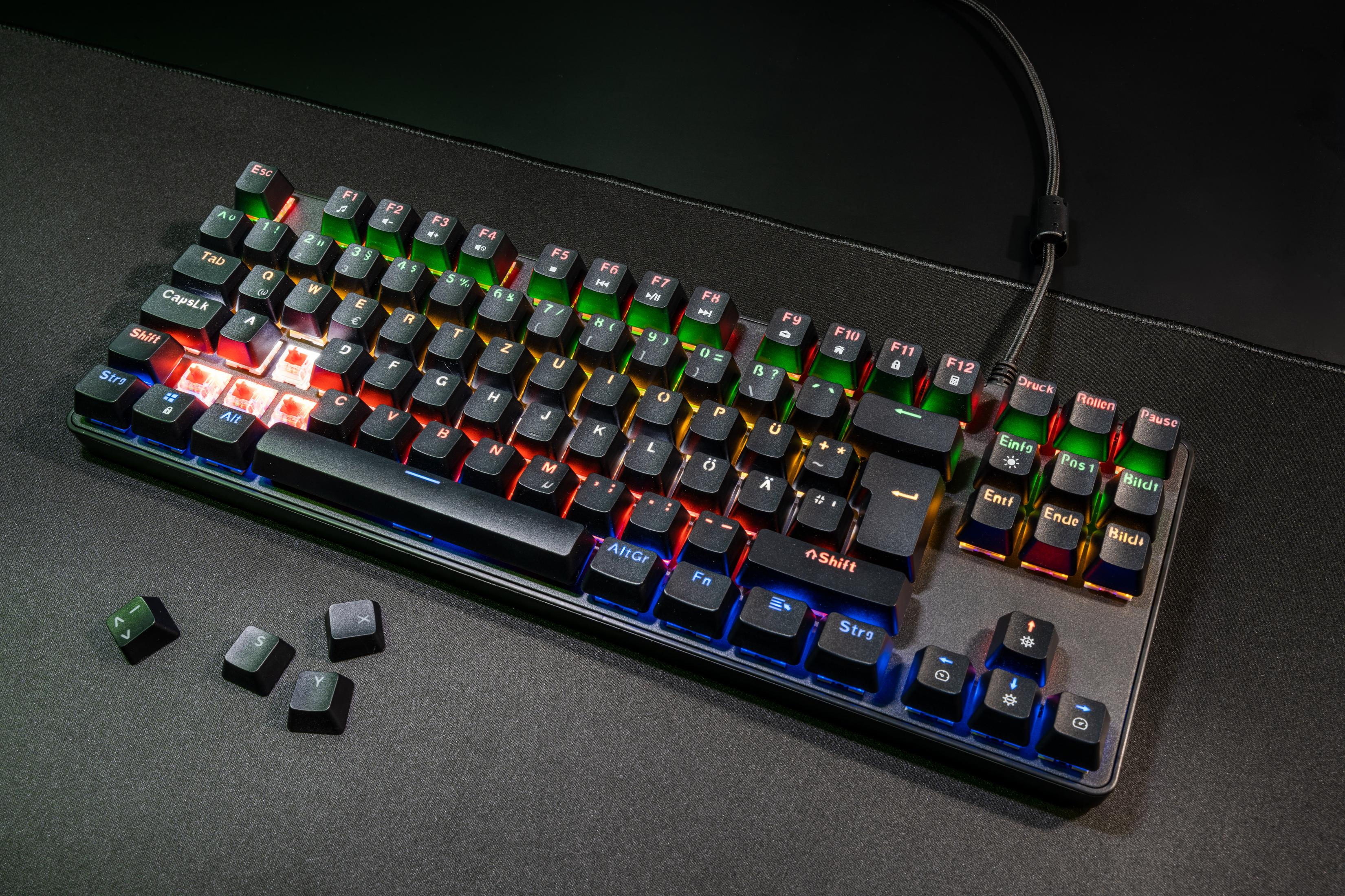 Schwarze Tastatur mit beleuchteten Tasten auf dunkler Oberfläche. Einige Tasten entfernt. Farben: rot, grün, blau.