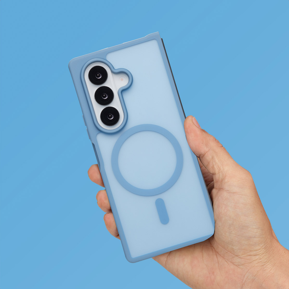 Een hand houdt een lichtblauwe telefoonhoes vast met een magnetische ring, tegen een lichtblauwe achtergrond.