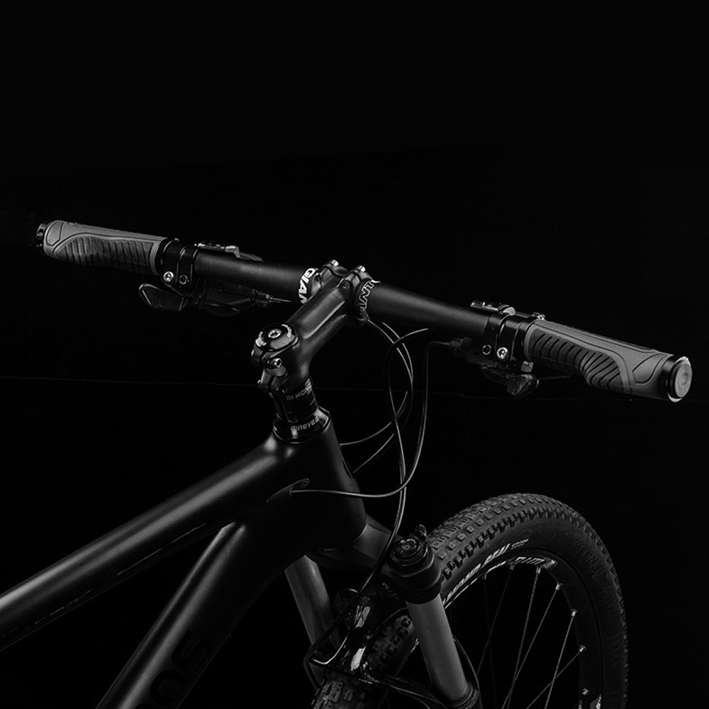 Czarna kierownica roweru z szarymi uchwytami na czarnym tle. Widoczna przednia opona.