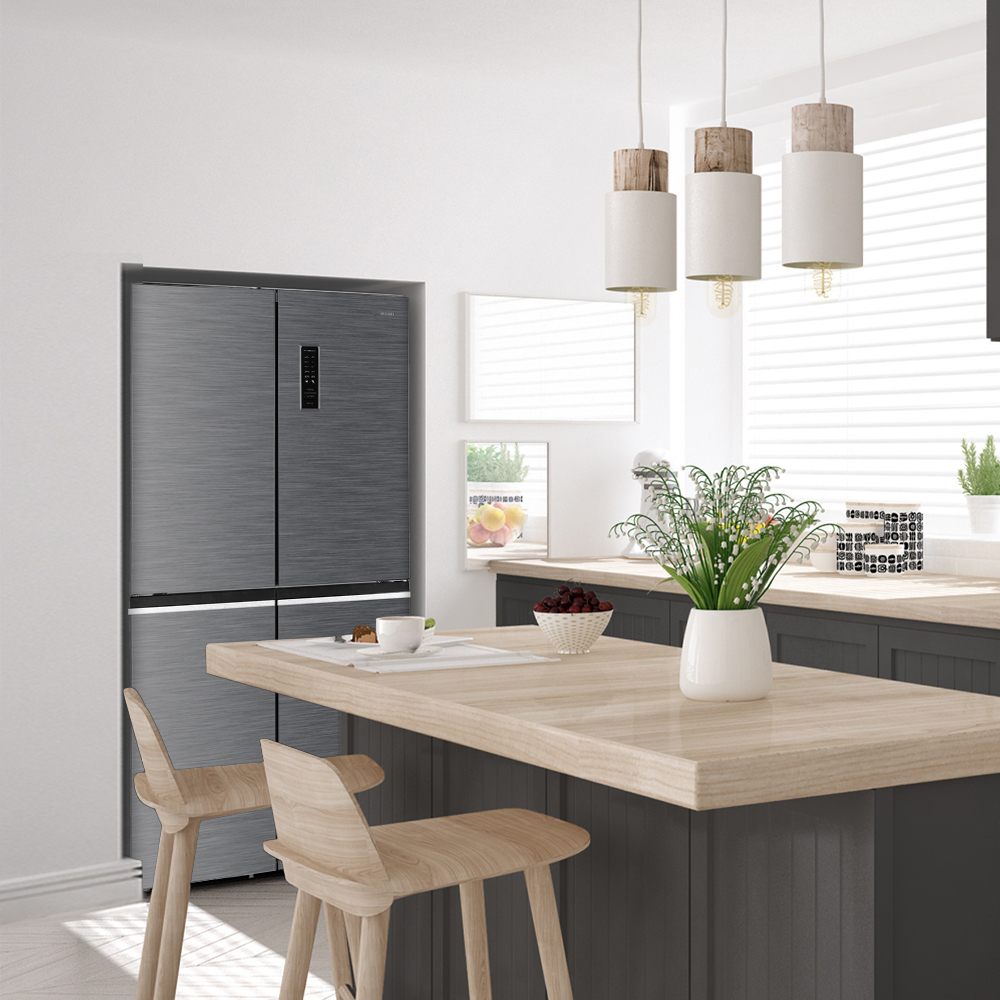 Un refrigerador gris está en una cocina moderna con detalles de madera, lámparas colgantes y una mesa con flores.