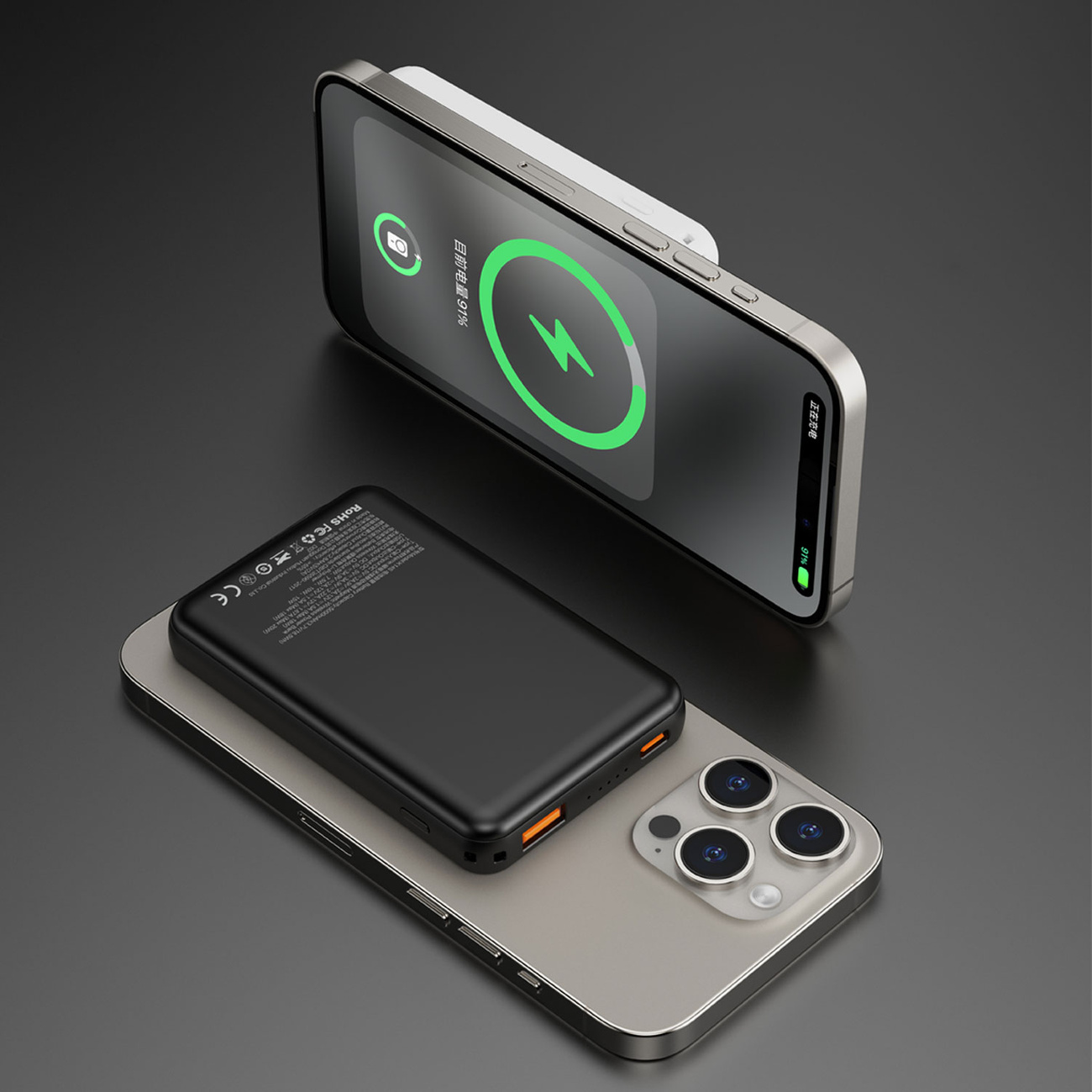 Czarny power bank na srebrnym telefonie, w trakcie ładowania. Drugi telefon na górze, ładujący się bezprzewodowo.