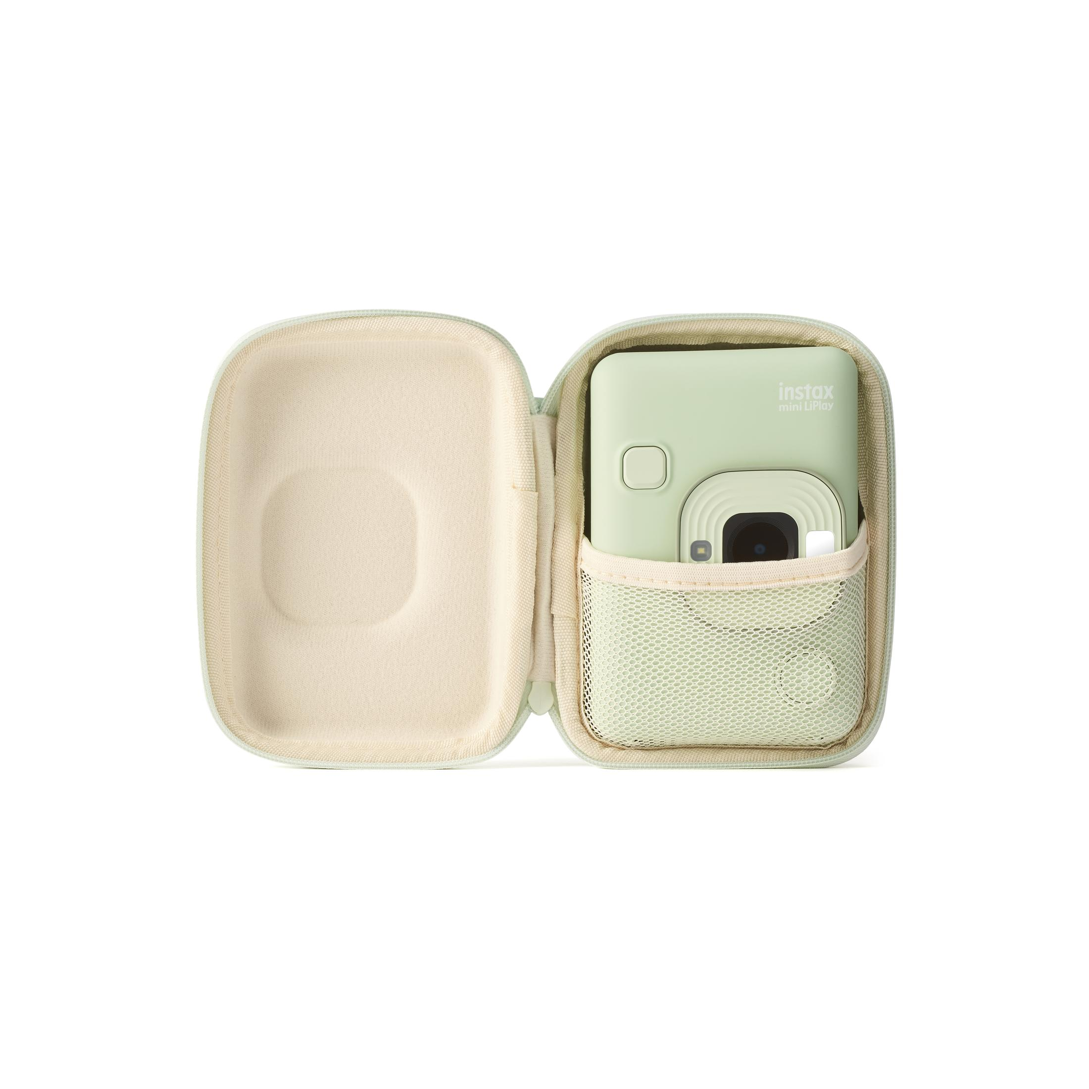 Estuche de cámara Instax verde claro abierto, con cámara dentro, sobre superficie blanca.