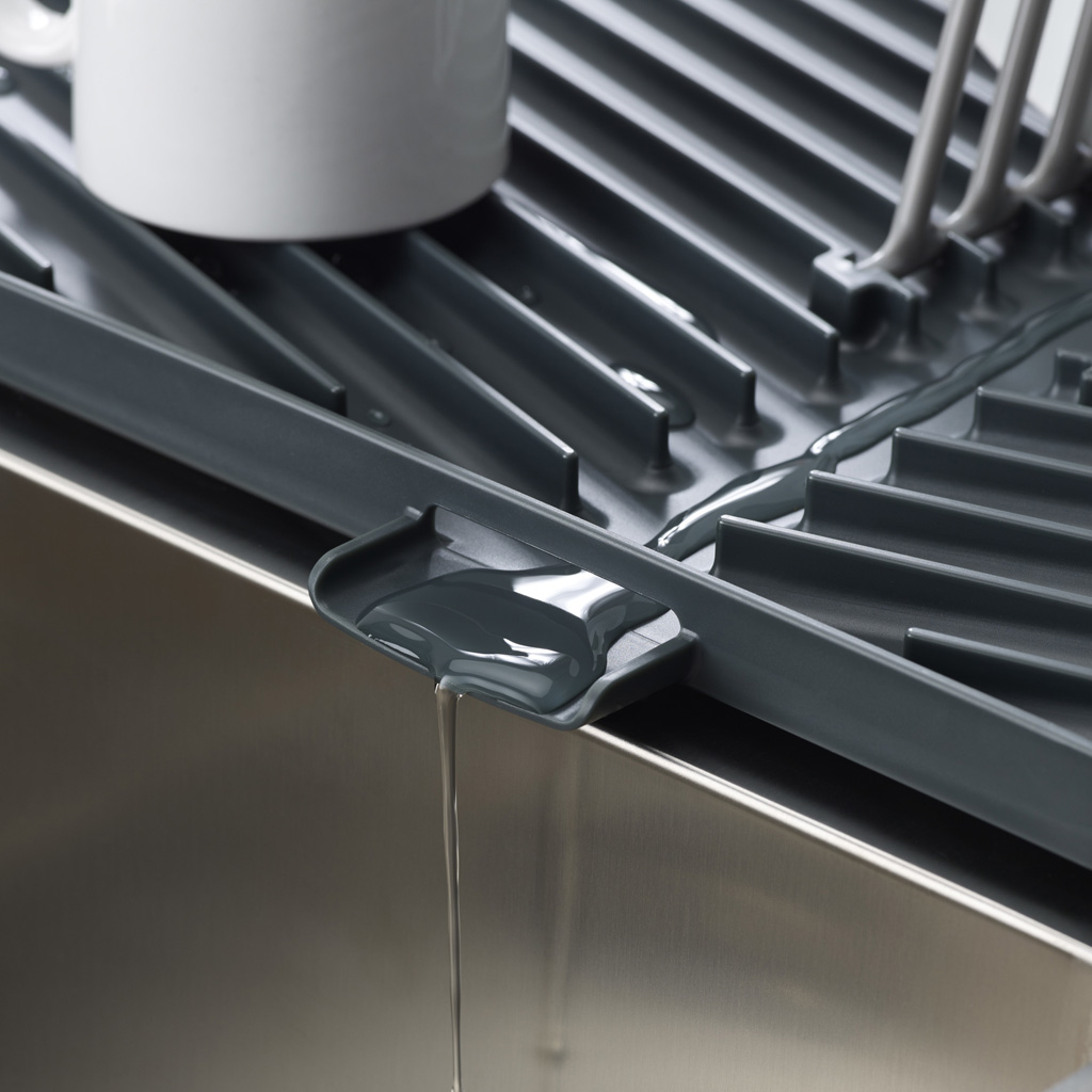 Primer plano de un escurridor gris que drena agua en un fregadero de acero inoxidable, mostrando un detalle de su sistema de drenaje.
