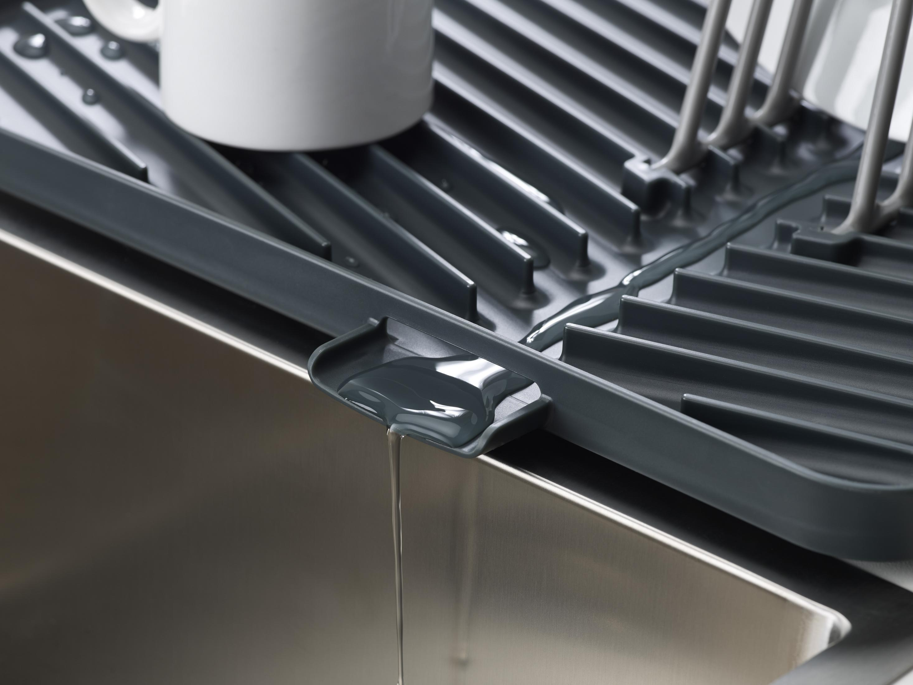 Primer plano del agua que drena de un escurridor gris a un fregadero de acero inoxidable, con una taza blanca visible.