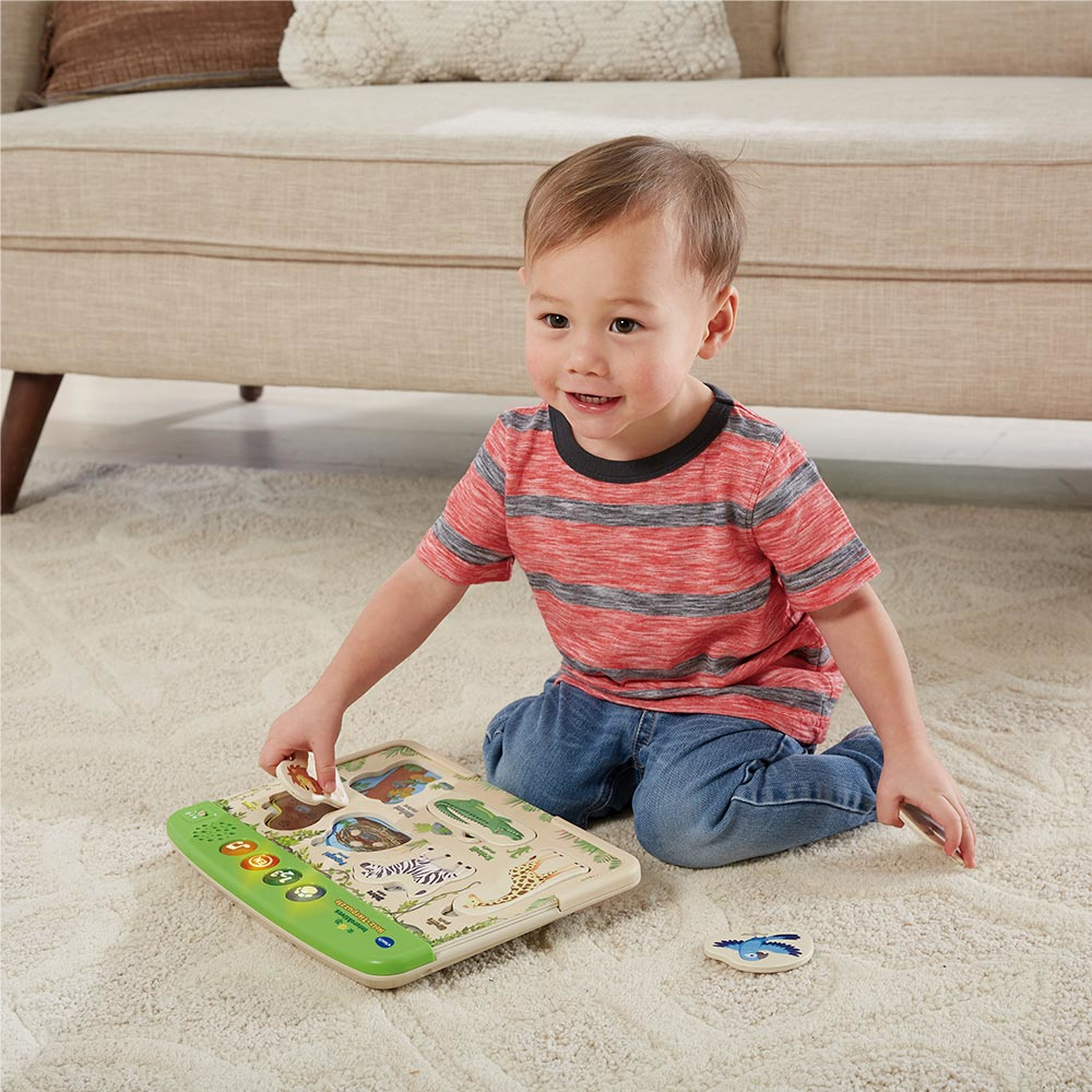Ein Kind spielt mit einem Tierpuzzle auf einem weißen Teppich vor einer Couch.