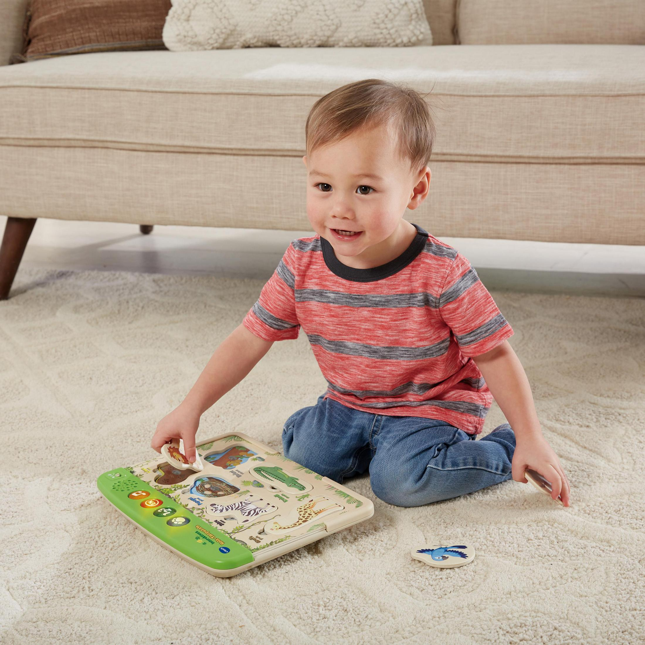 Kleinkind spielt mit einem interaktiven Tierpuzzle auf einem cremefarbenen Teppich in der Nähe eines beigen Sofas.