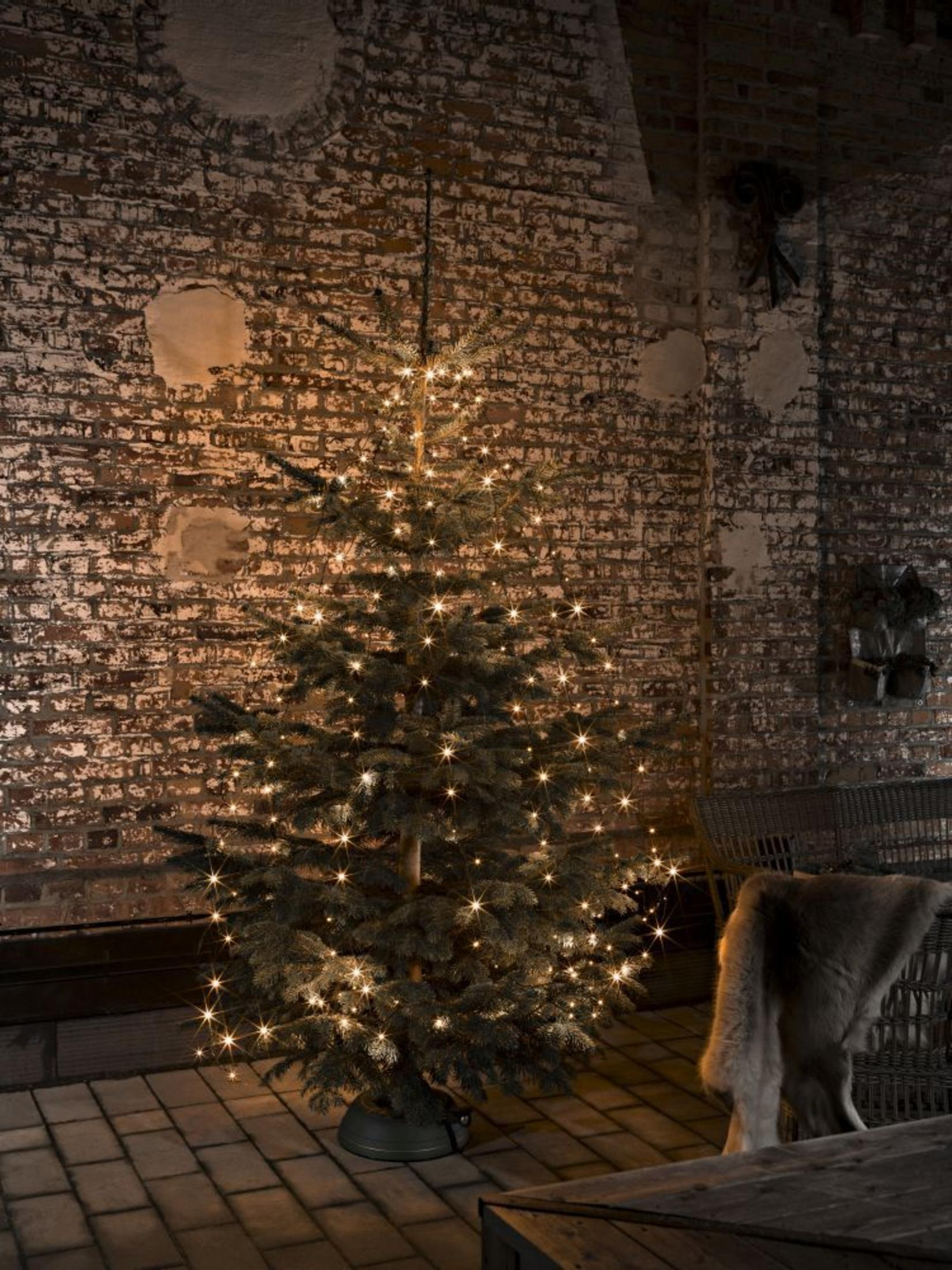 Ein Weihnachtsbaum mit Lichtern in einem Raum mit einer Ziegelmauer und einem Pelzüberwurf. Die Lichter sind warm und gelb.