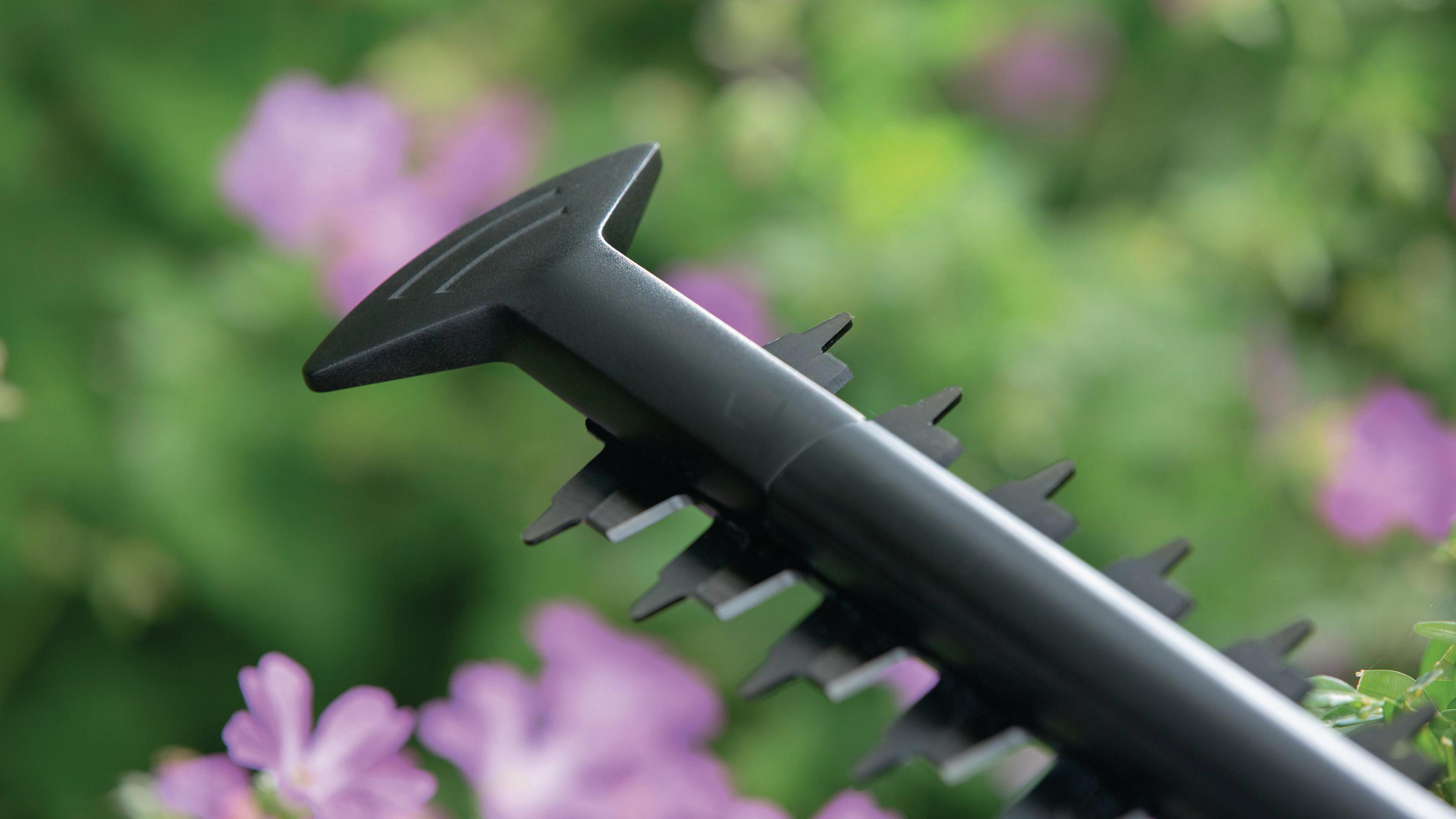 Nahaufnahme der Heckenscherenblätter. Die Klingen sind schwarz, mit verschwommenem floralen Hintergrund.