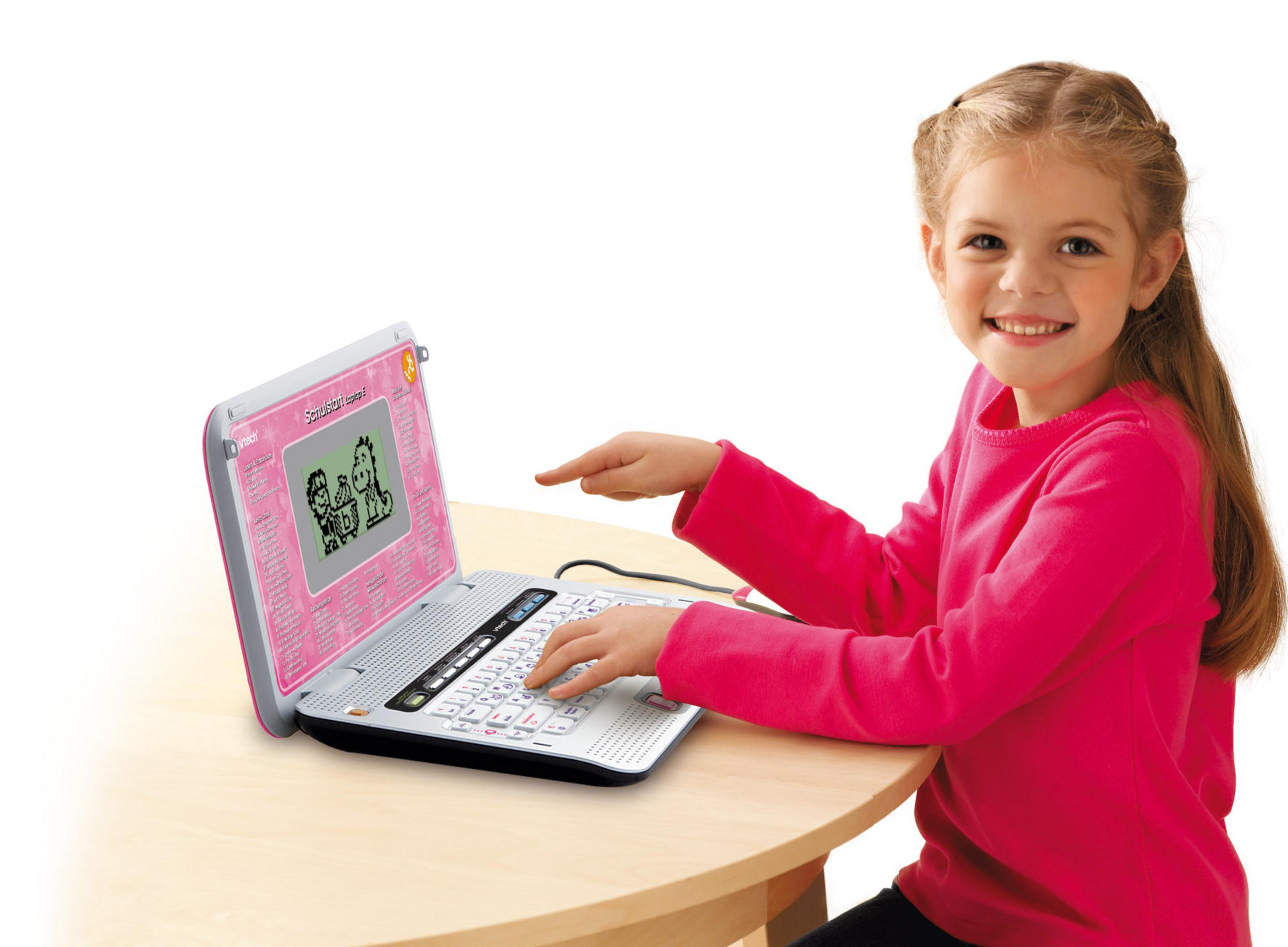 Ein Kind lächelt und benutzt einen rosa Spielzeug-Laptop auf einem Holztisch.
