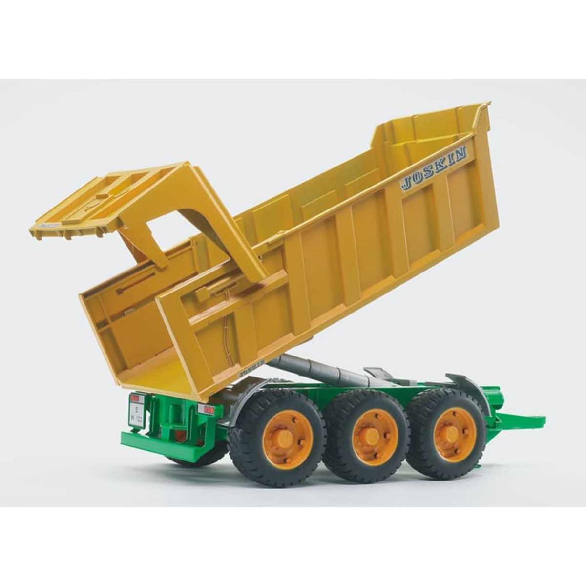 Un remolque amarillo Joskin inclinado sobre un chasis verde con ruedas grandes, sobre blanco.