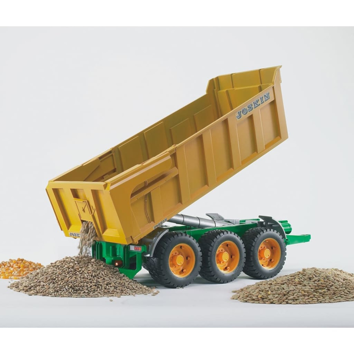 Un remolque amarillo Joskin inclinado con grano derramado, sobre chasis verde y ruedas grandes.