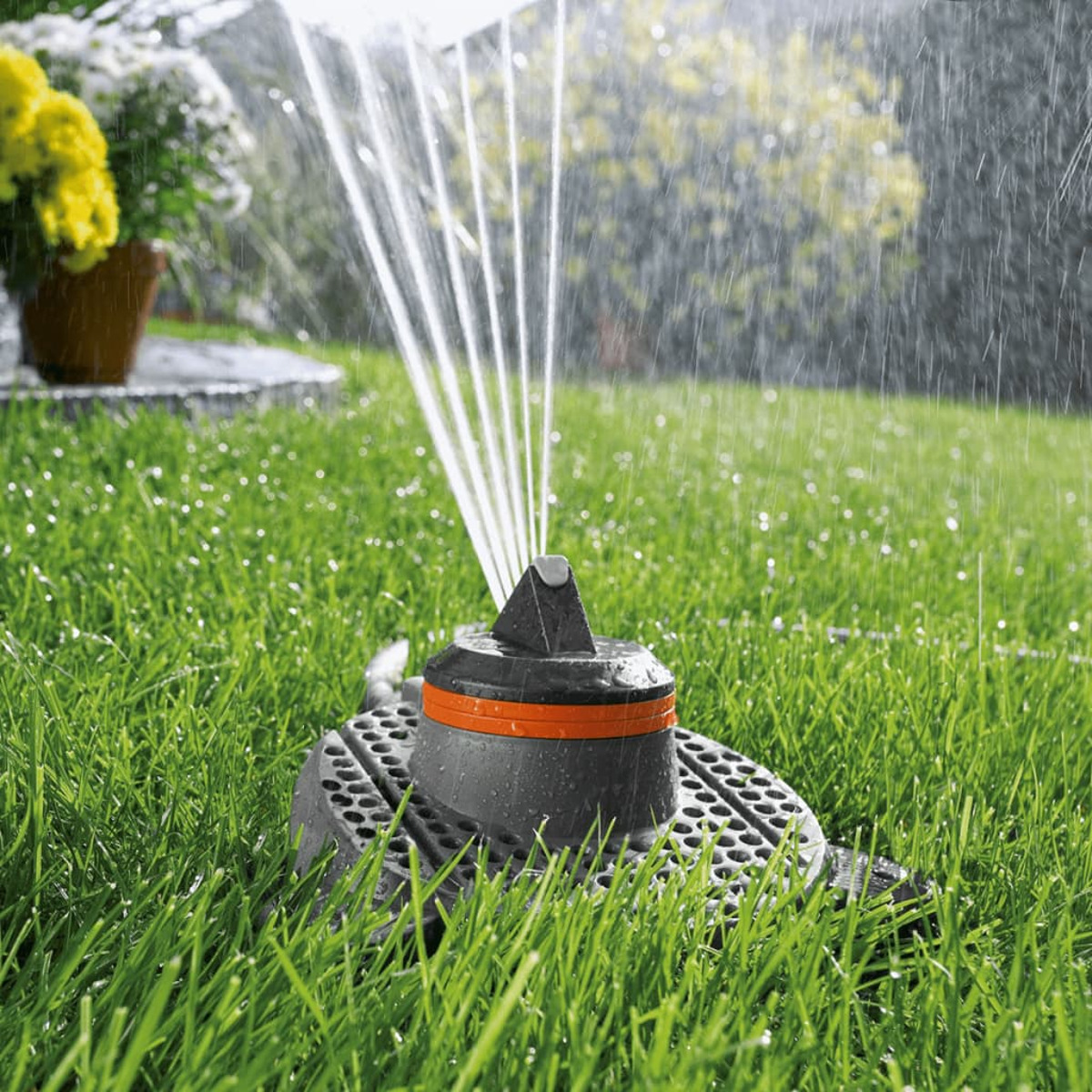 Ein Rasensprenger, der Wasser auf grünes Gras sprüht. Bäume und Büsche im Hintergrund.