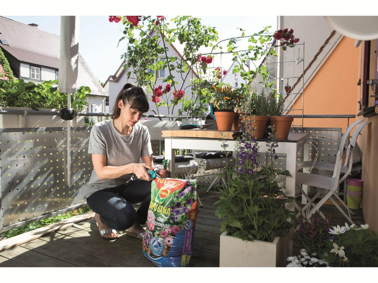 Eine Frau auf einem Balkon mit einem Beutel Erde und Pflanzen bereitet sich auf die Gartenarbeit vor.