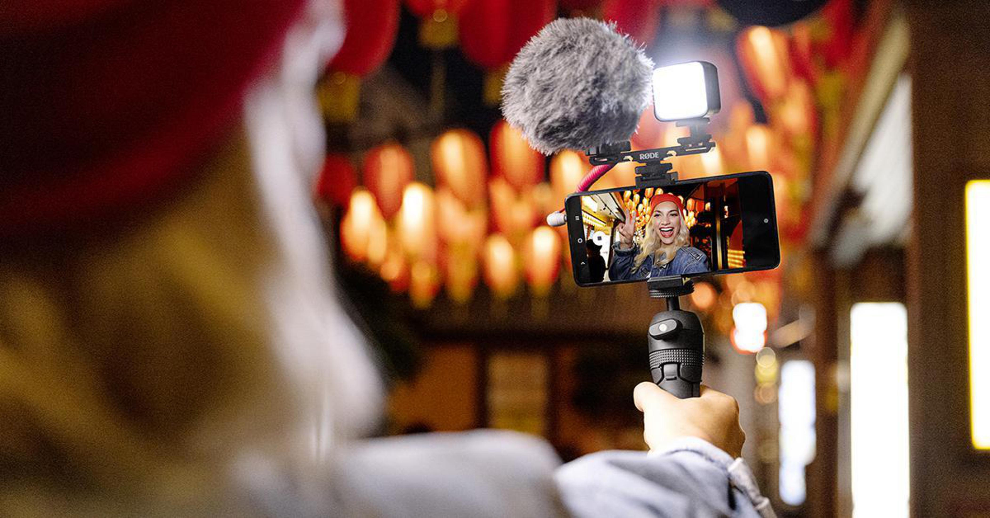 Persona che filma con smartphone. Telefono con luce e microfono. Sfondo sfocato con lanterne.
