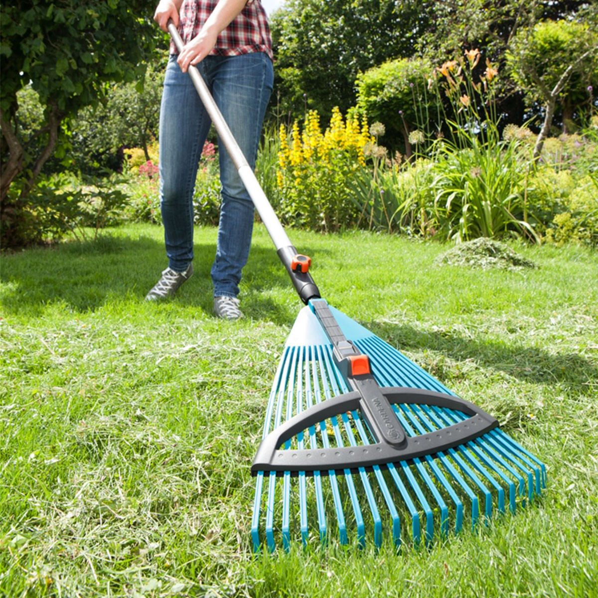 Una persona che rastrella l'erba con un rastrello GARDENA blu e nero.