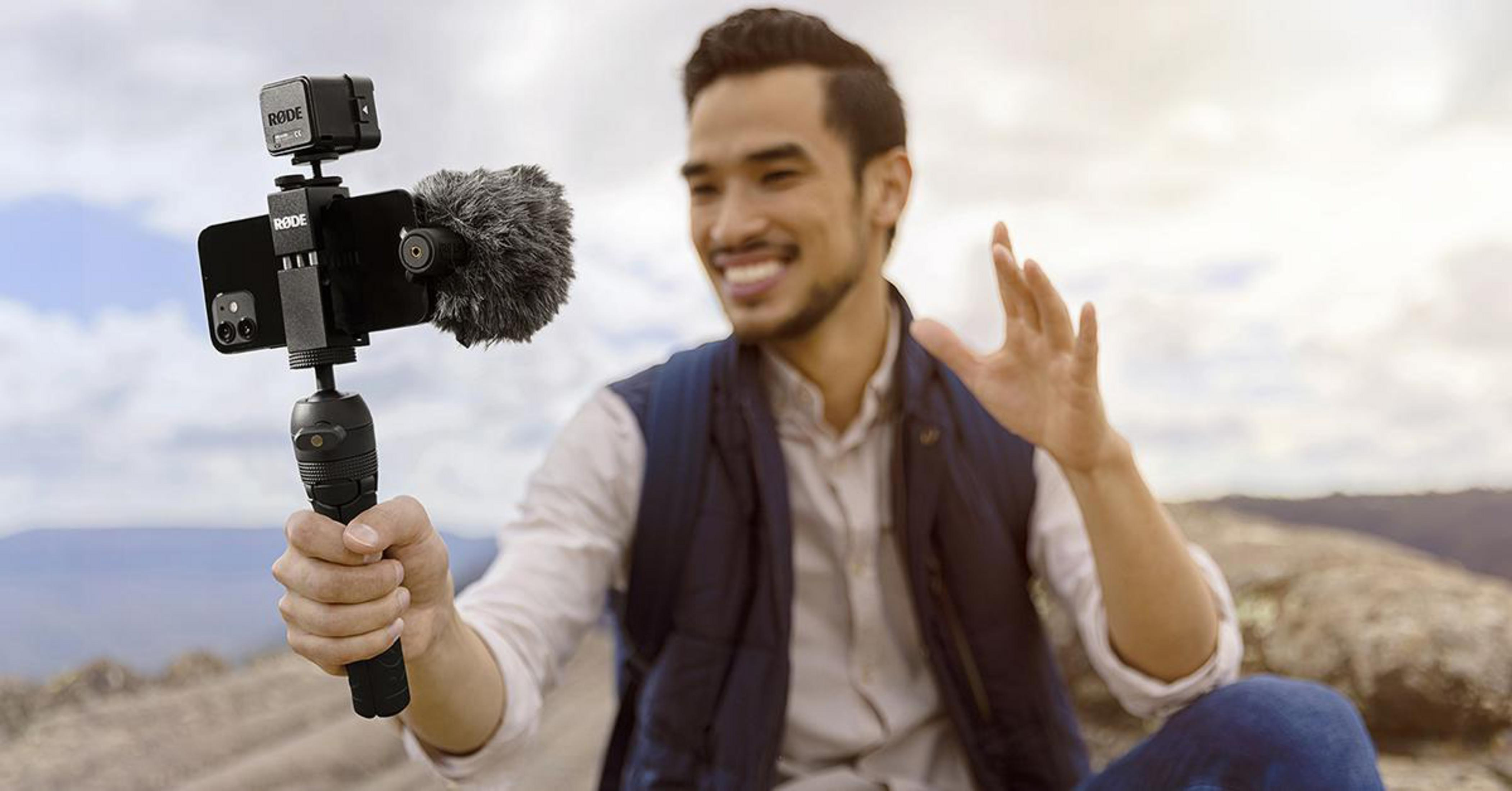 Un uomo sorridente tiene in mano un telefono con un kit di vlogging attaccato all'aperto.