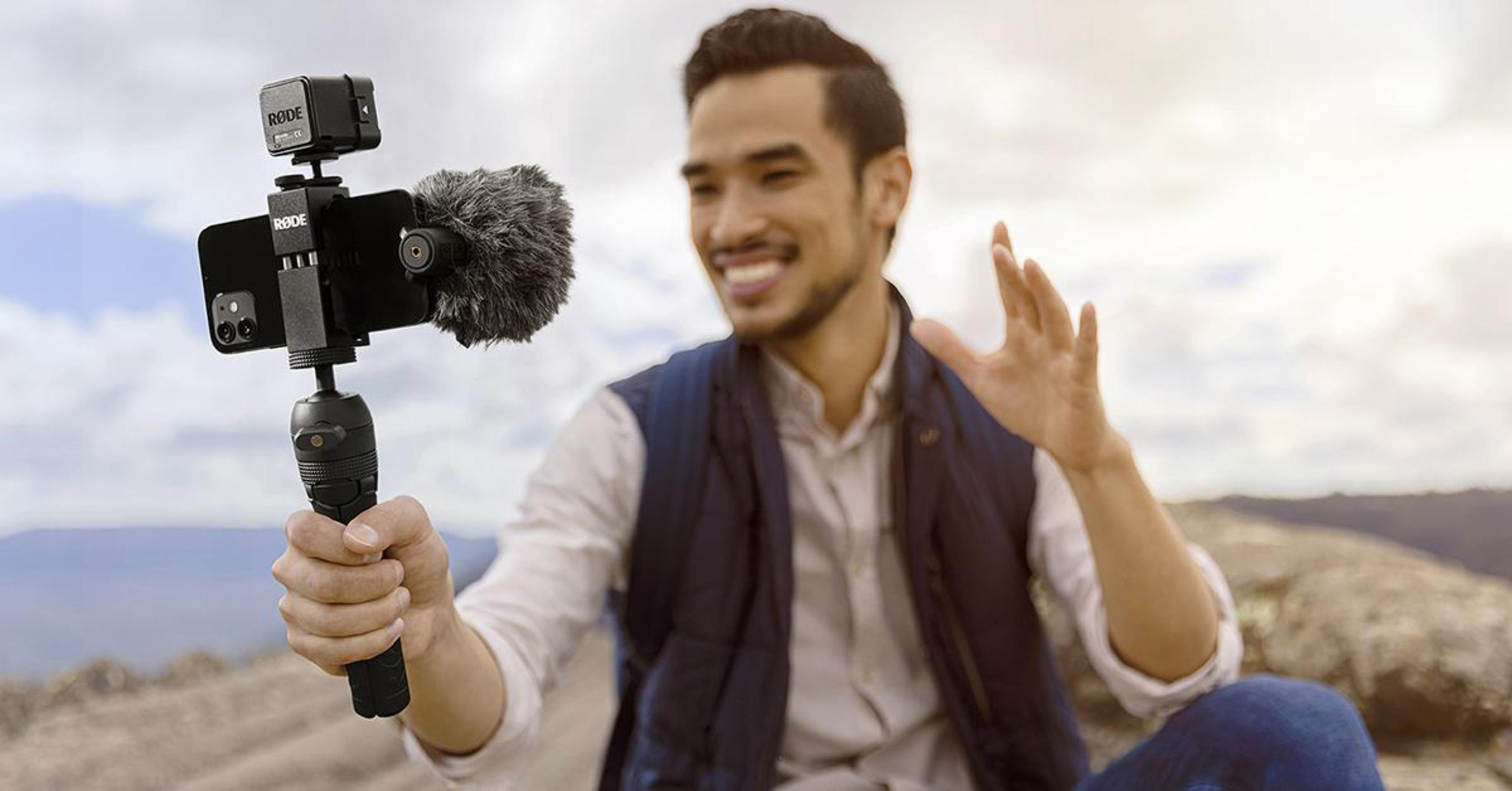 Un uomo sorridente tiene in mano un telefono con un kit di vlogging attaccato all'aperto.