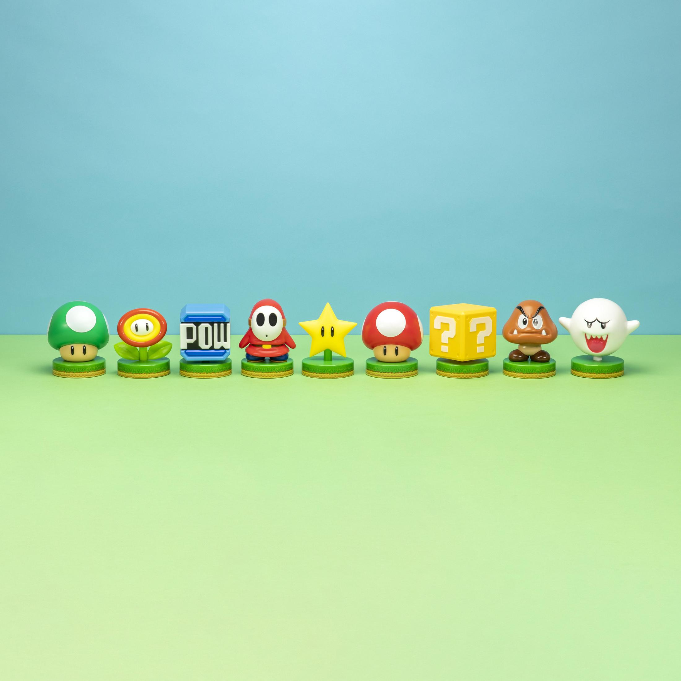 Linia ośmiu figurek Mario, w tym gwiazda, grzyb i blok POW, na zielonej powierzchni.