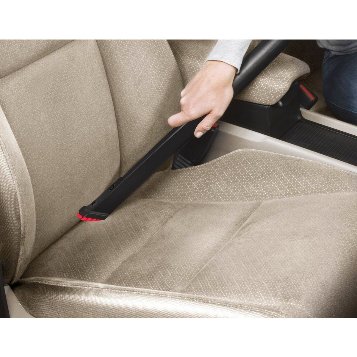 Person reinigt Autositz mit Staubsaugeraufsatz. Beiges Interieur.