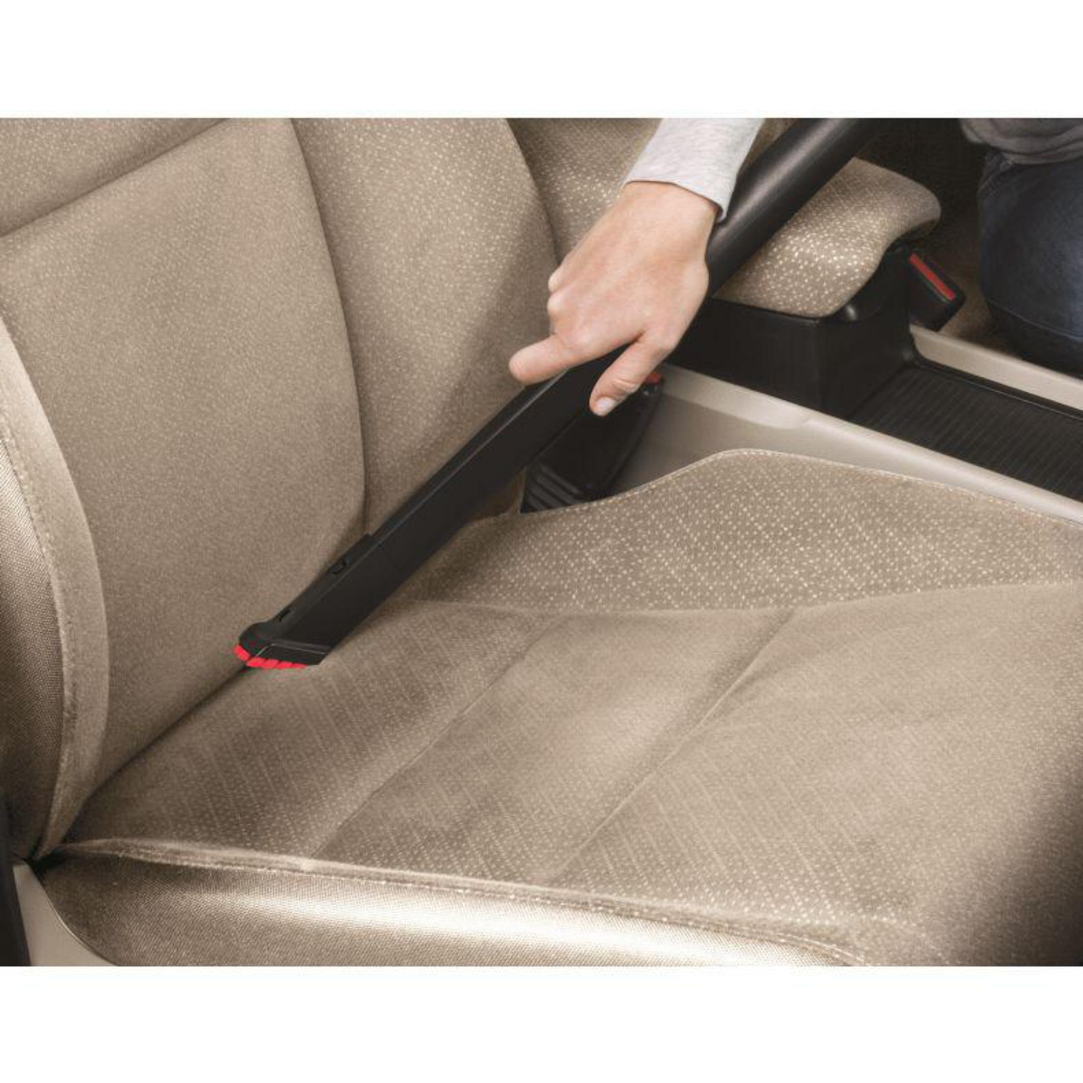 Persona usa accessorio aspirapolvere per pulire sedile auto. Interni beige.