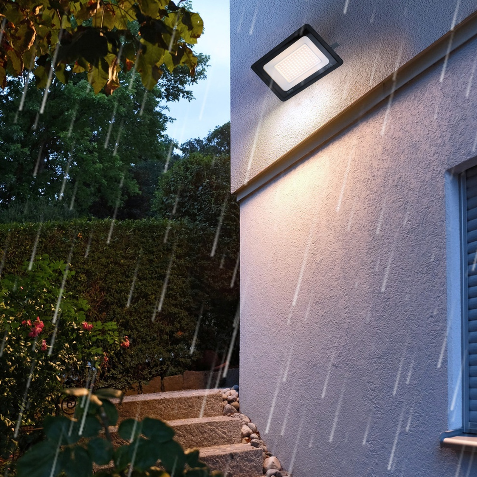 Un foco instalado en una pared, con lluvia cayendo. La luz ilumina el área alrededor de la pared.