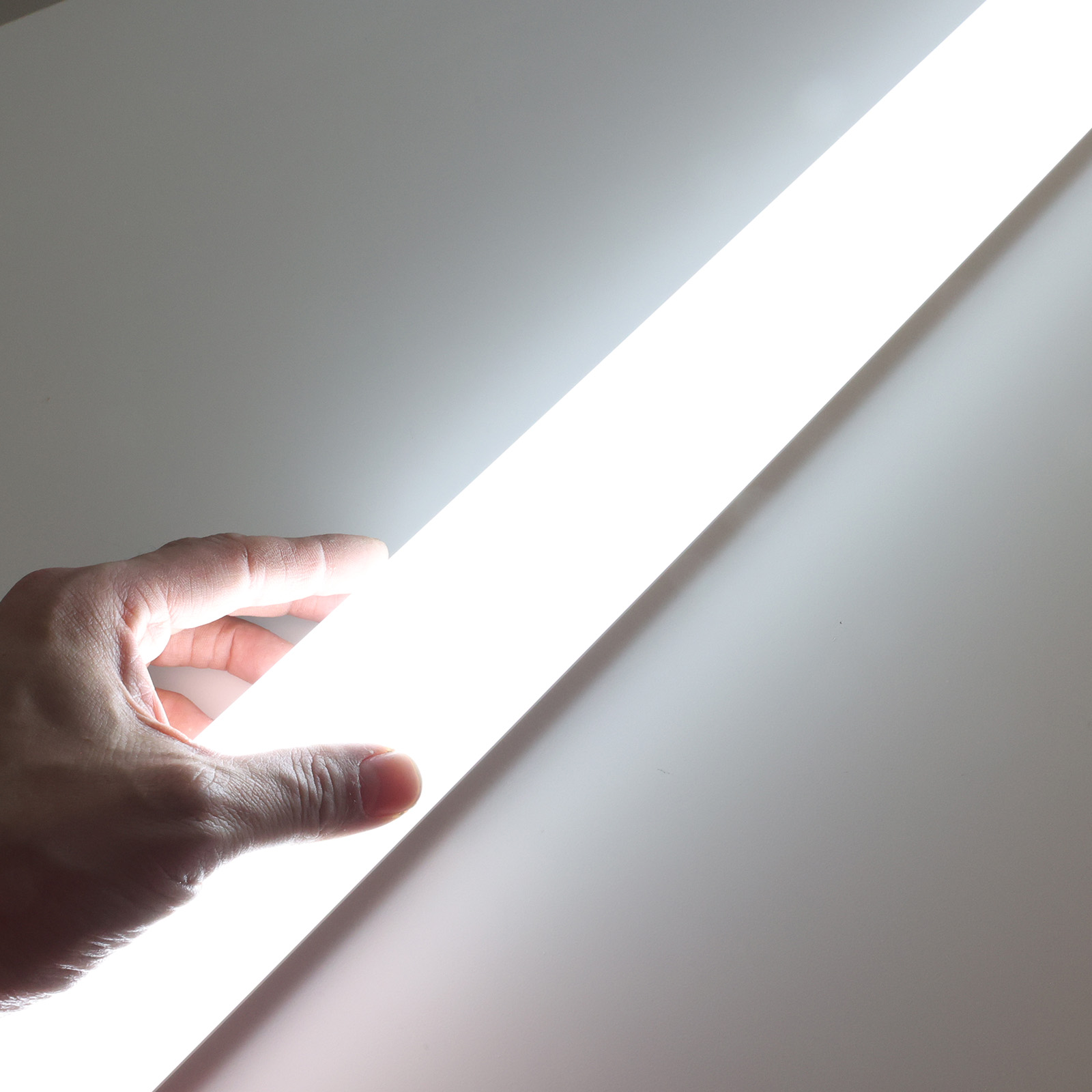 Una mano sostiene una barra de luz LED blanca brillante, iluminando la palma y los dedos contra un fondo claro.