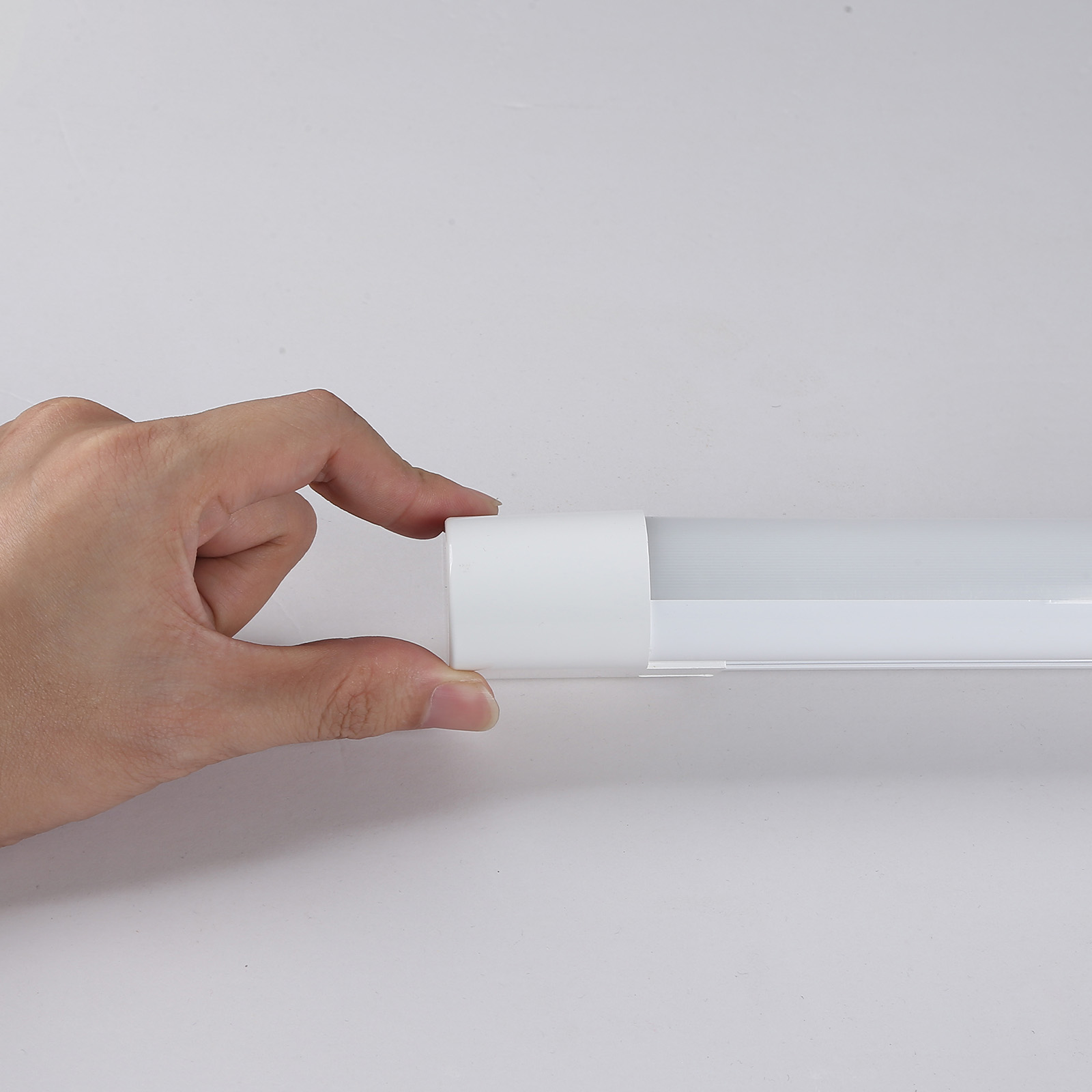 Una mano sosteniendo el extremo de una barra de luz blanca. El fondo es blanco.