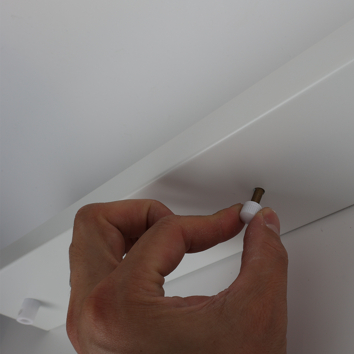 Se muestra una mano instalando un tornillo blanco en una placa de montaje blanca.
