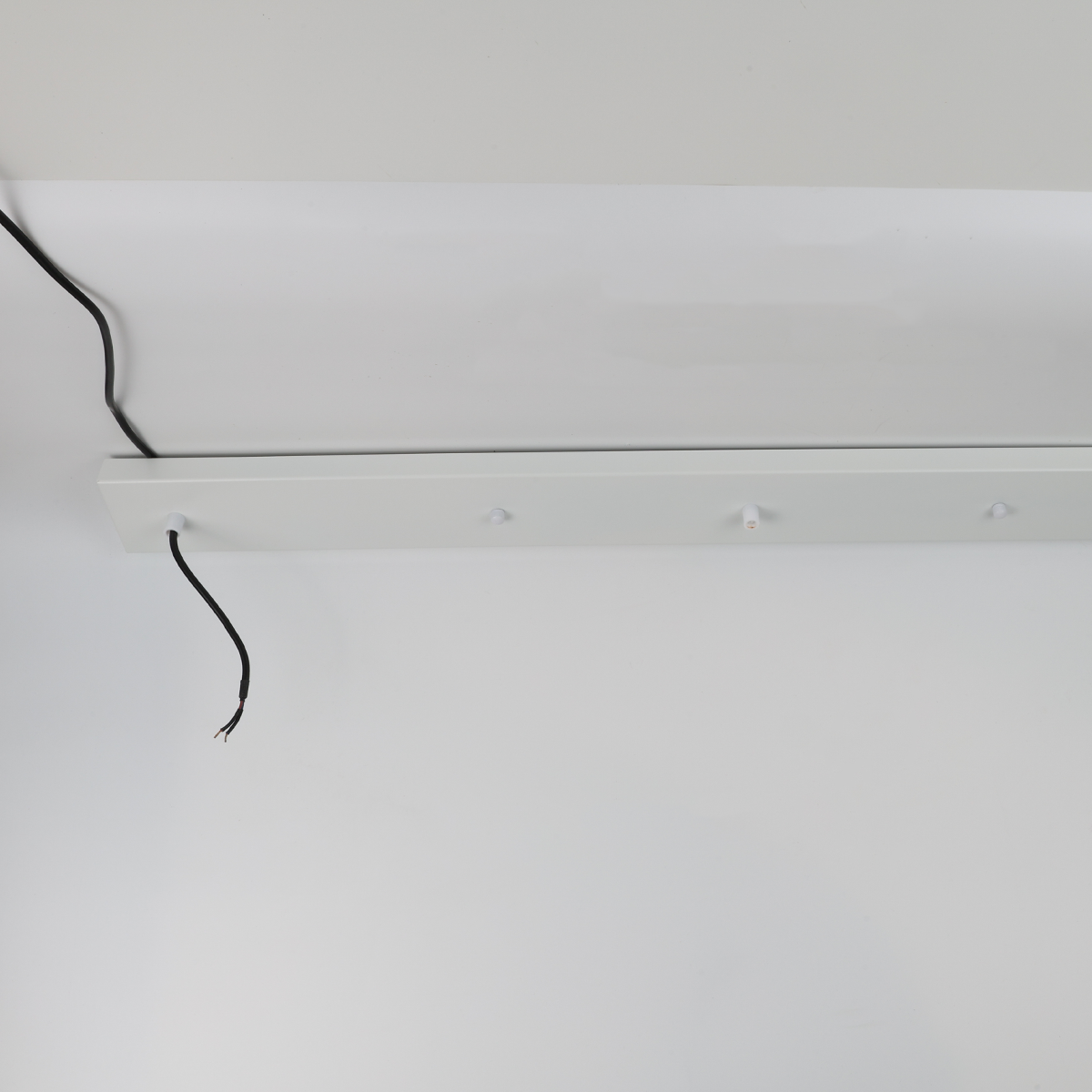 Se muestra una placa de montaje blanca con cables sueltos contra una pared blanca.
